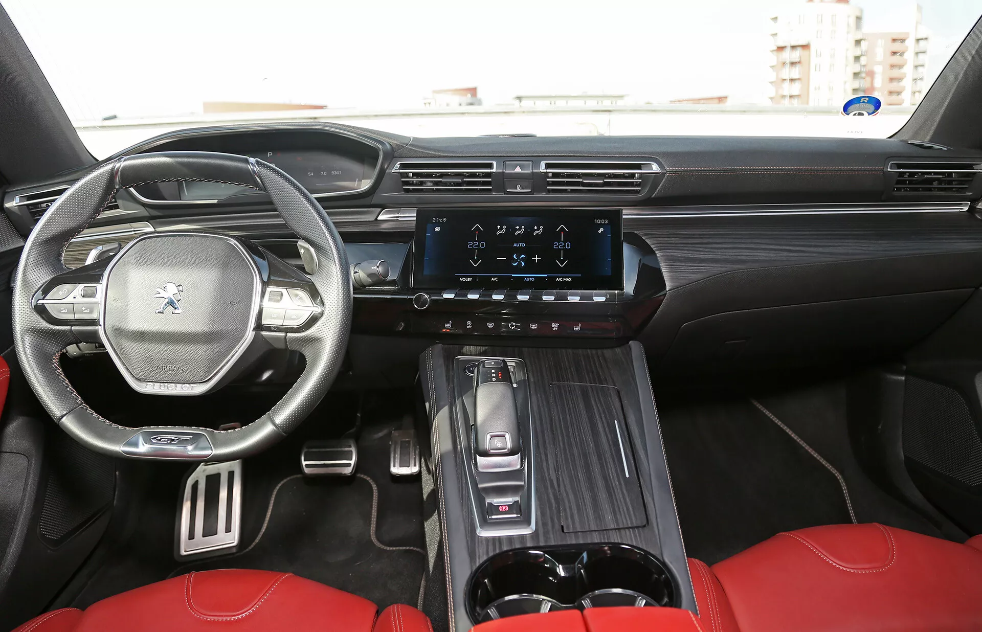 Vue intérieure d'une Toyota Camry 2001 (Camry-Limousine) montrant la cabine avant depuis la perspective du siège arrière avec un tableau de bord détaillé, sièges avant à garniture rouge, volant avec logo, système d'infodivertissement affichant la commande de climatisation, levier de vitesse automatique et accents de luxe en grain de bois
