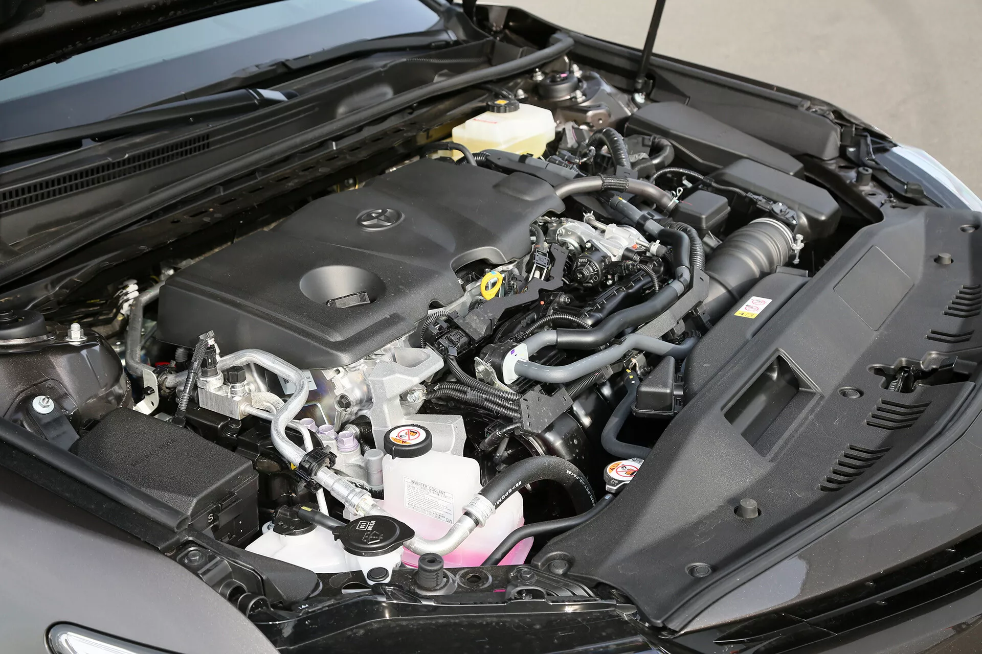 Vue rapprochée du compartiment moteur d'une Toyota Camry Limousine 2001 montrant le couvercle du moteur, le collecteur d'admission, les connecteurs électriques, le réservoir de liquide de refroidissement, et le tuyau d'admission d'air