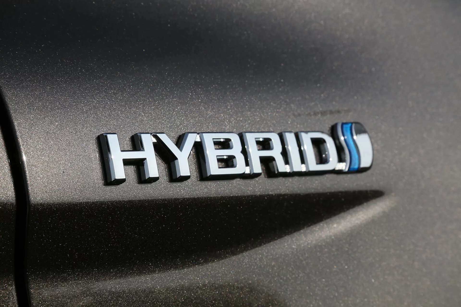 Gros plan sur un badge hybride Toyota Camry 2001 avec des accents de chrome et bleu, mettant en avant la technologie hybride écologique sur la carrosserie d'une voiture sous un éclairage naturel.