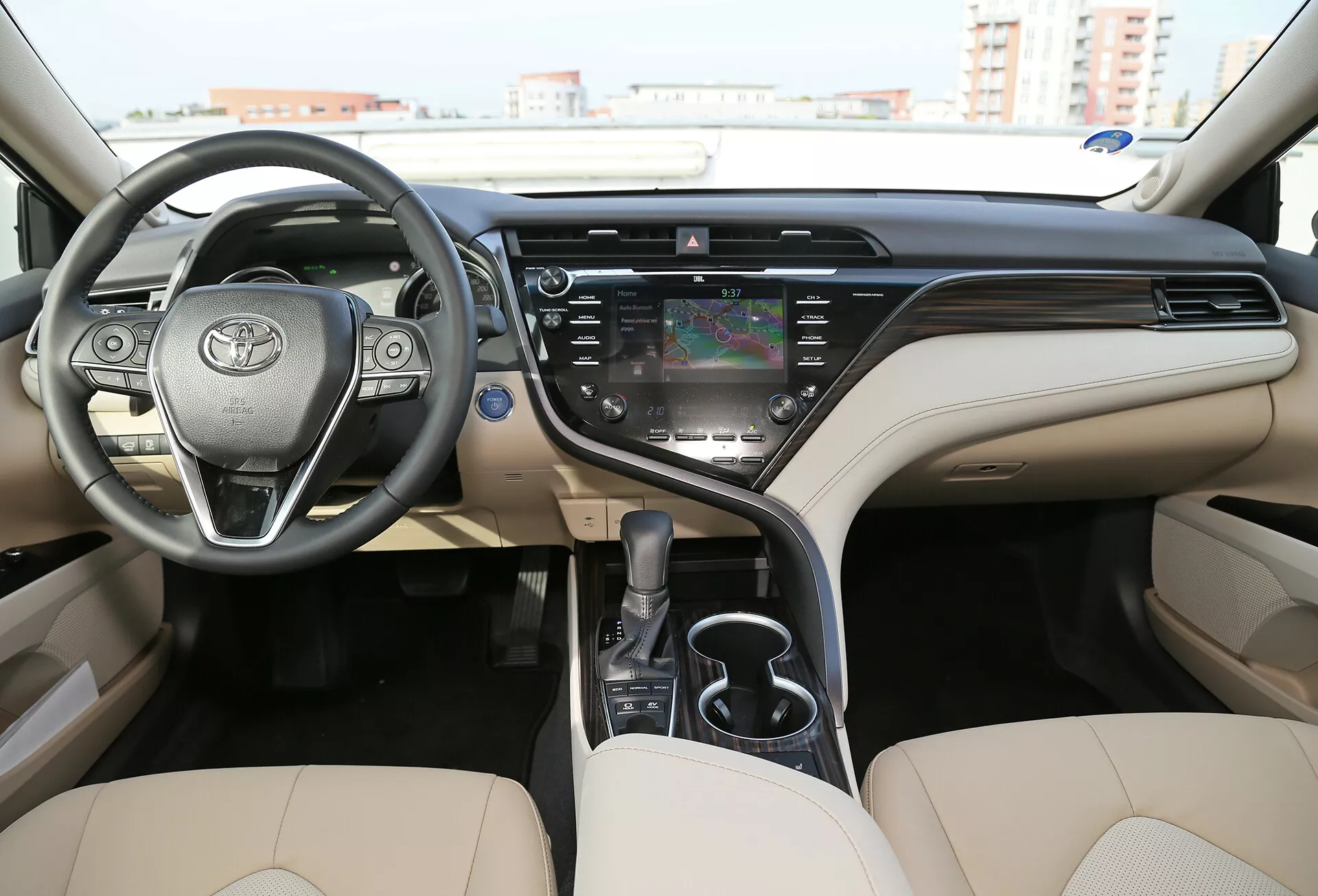 Vue intérieure de la limousine Toyota Camry 2001 mettant en avant le tableau de bord, le volant avec commandes intégrées, et les sièges avant dans un schéma bicolore avec composants numériques et analogiques, écran tactile central pour l'infodivertissement et finition haut de gamme.
