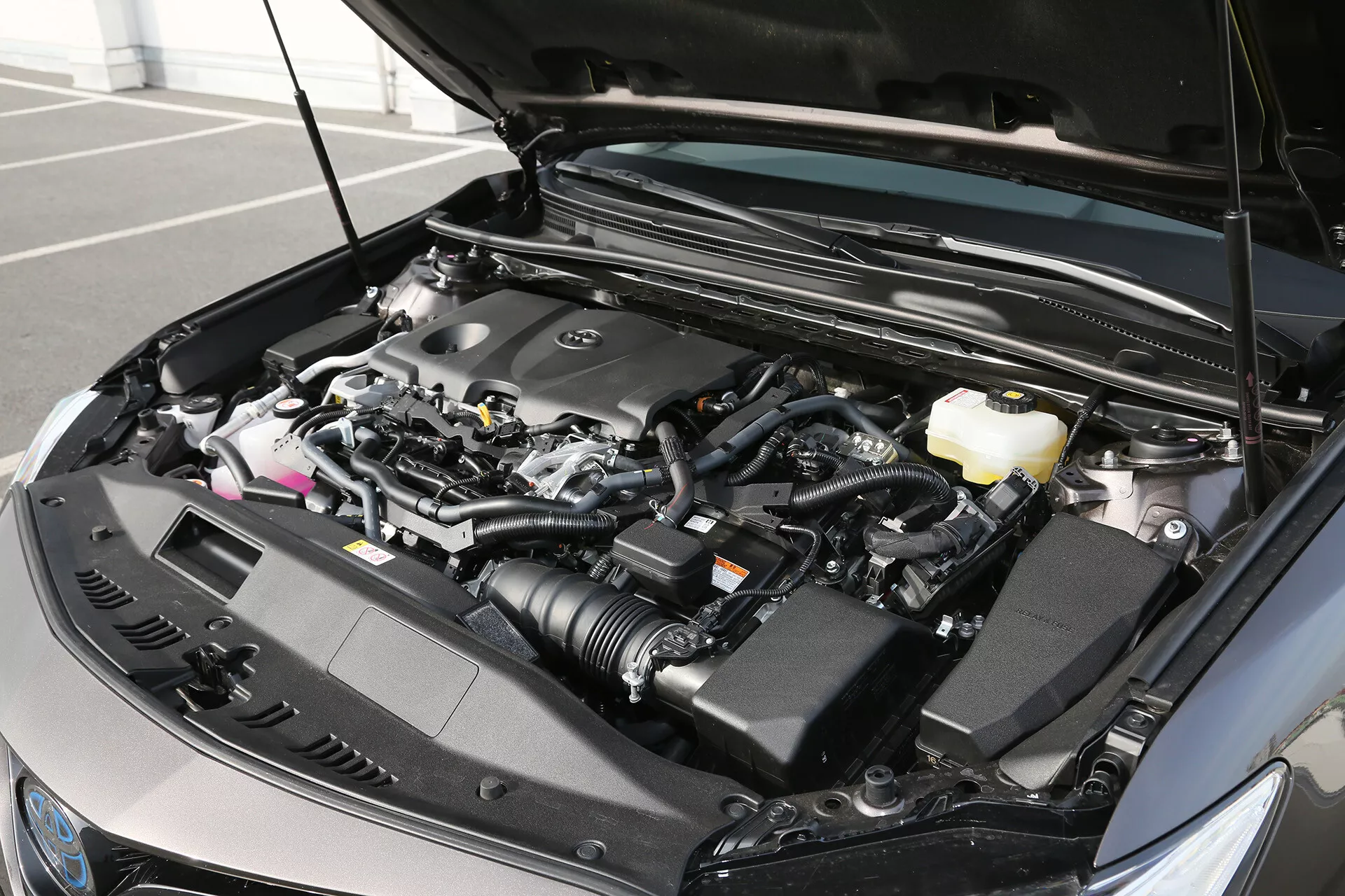 Photo en gros plan du compartiment moteur d'un véhicule moderne montrant des composants technologiques avancés, prise depuis un angle moyen-gauche avec le capot ouvert, révélant des détails du moteur et divers réservoirs de systèmes indiquant une conception post-2010