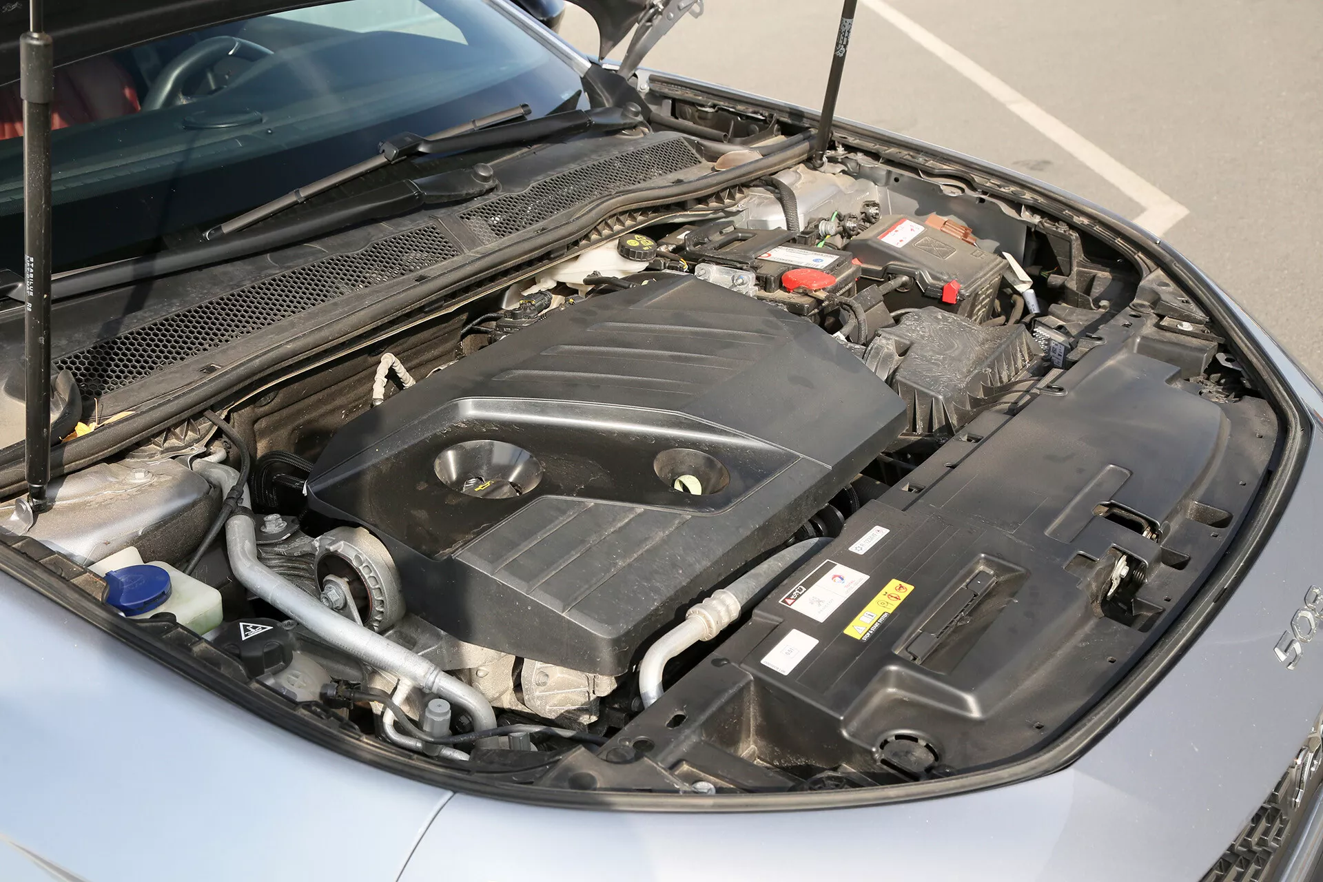 Vue rapprochée sous le capot d'une limousine Toyota Camry 2001, présentant son compartiment moteur avec une claire visibilité de la batterie, du réservoir de liquide de refroidissement avec un bouchon bleu, et de divers points de maintenance pendant la journée sous un éclairage naturel
