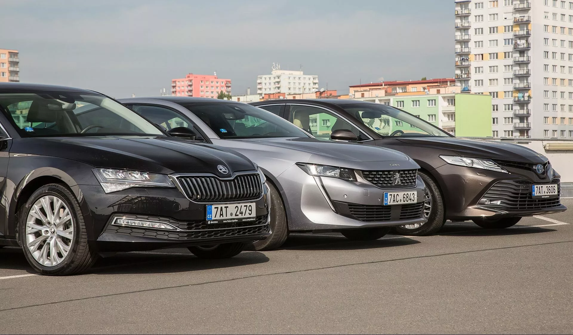 Gamme Toyota Camry 2019, comprenant des modèles de couleur sombre, argent et gris dans un cadre urbain, offrant une vue de trois quarts avant avec phares LED et éléments de design soignés