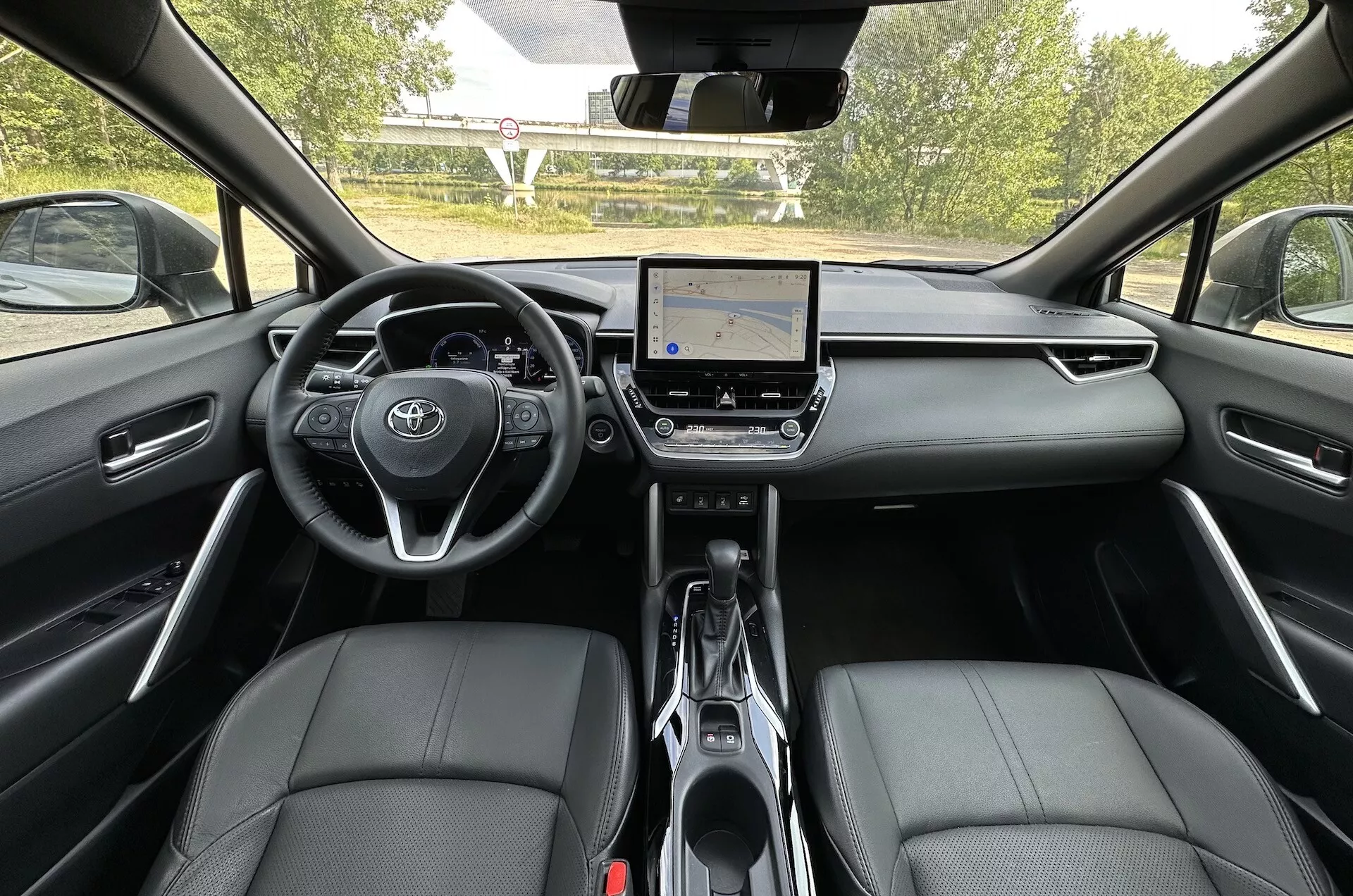 Vue intérieure de la Toyota Corolla Cross 2022 depuis le siège arrière montrant le tableau de bord, le système d'infodivertissement tactile et les sièges avant en cuir