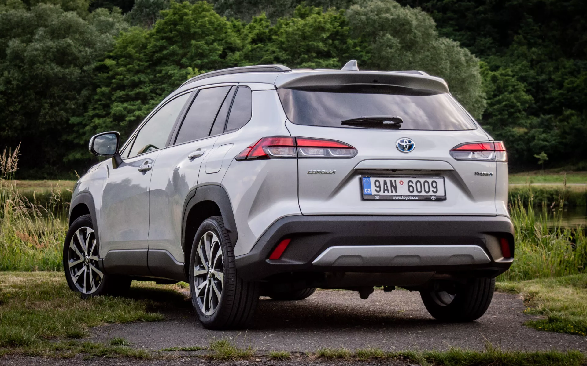 Vue arrière trois quarts de la Toyota Corolla Cross 2022 montrant les feux arrière LED, le badge hybride et les capteurs d'aide au stationnement