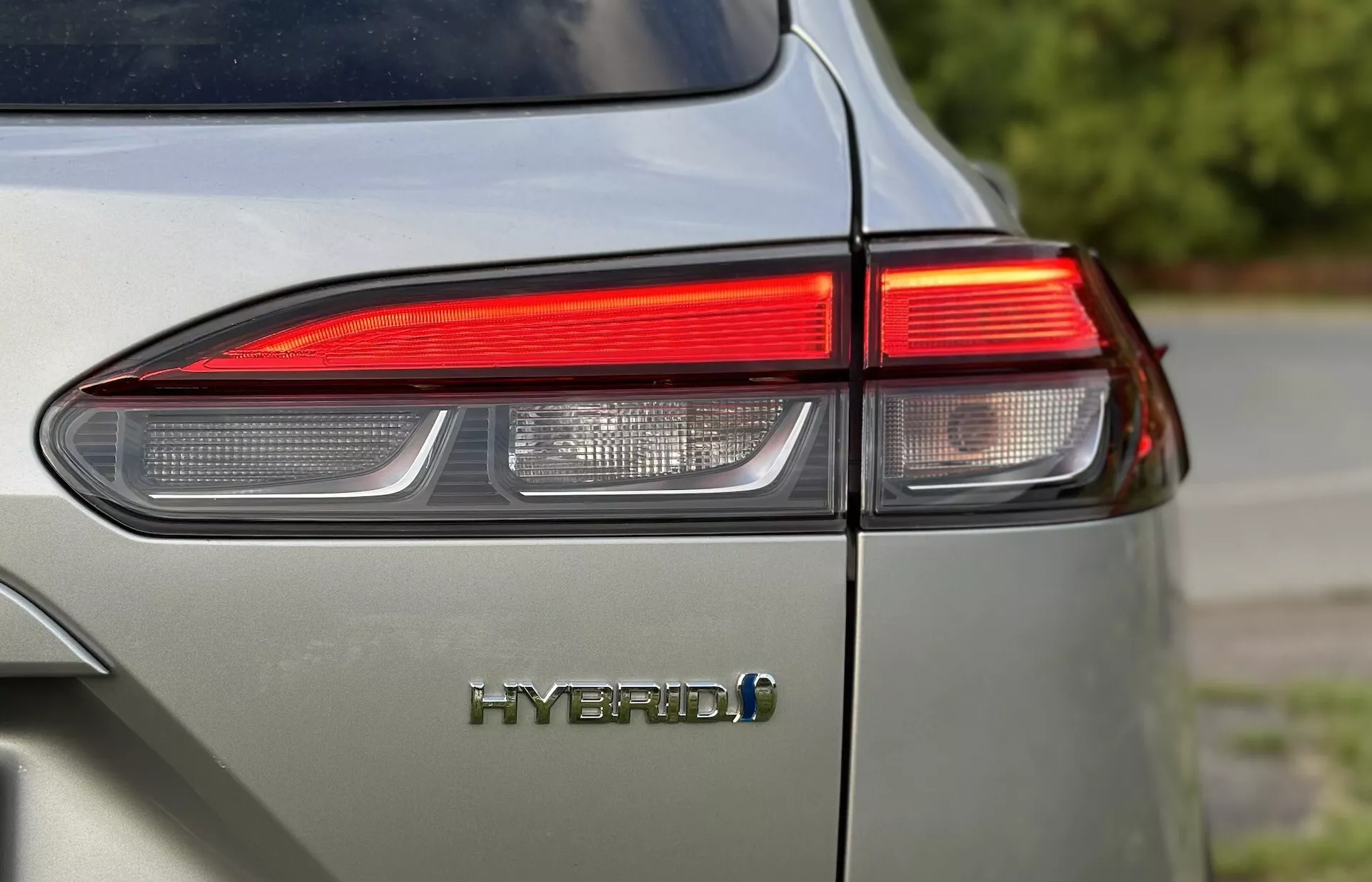 Gros plan sur le coin arrière gauche de la Toyota Corolla-Cross 2022 montrant le design du feu arrière LED et l'emblème HYBRID avec un accent sur la technologie respectueuse de l'environnement du véhicule et une finition brillante dans une couleur gris clair