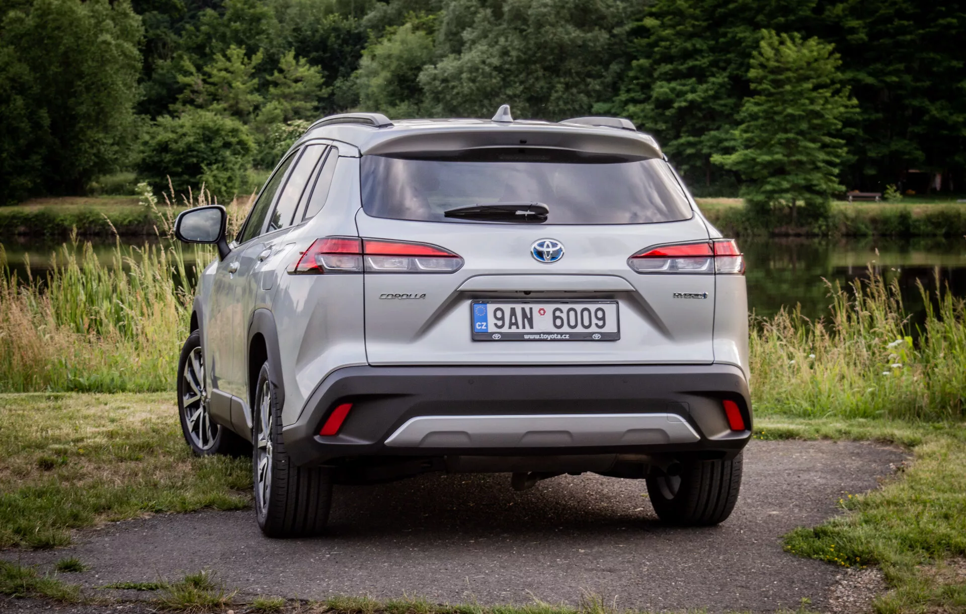 Toyota Corolla Cross argentée de 2022 garée sur un pavé avec de la verdure en arrière-plan montrant ses feux arrière LED, son spoiler arrière, sa roue en alliage à plusieurs branches et son badge hybride à la lumière naturelle du jour