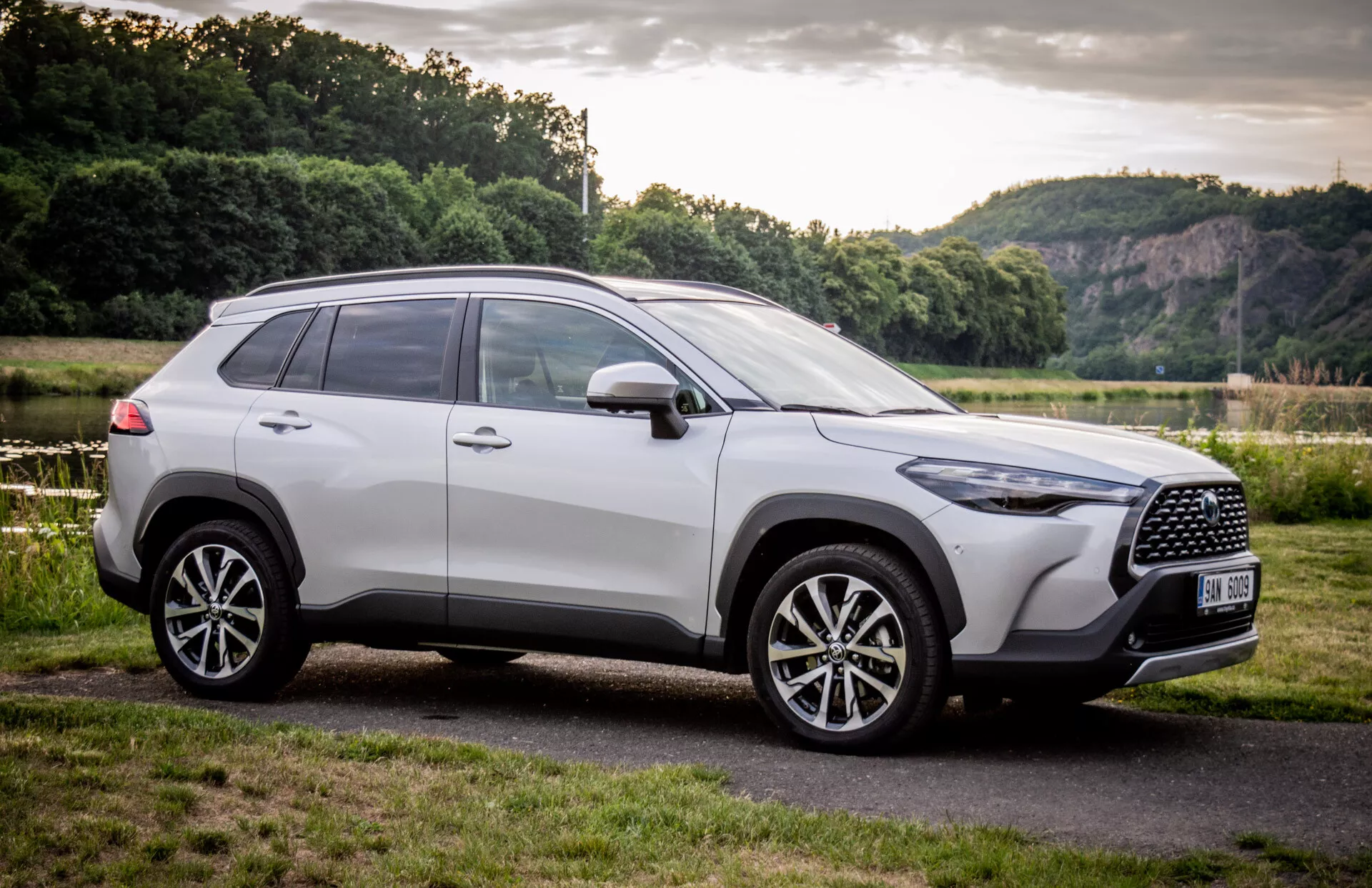 SUV Toyota Corolla Cross 2022 garé en plein air, présentant son design moderne sous un angle frontal de trois quarts avec un focus sur la grille, les roues en alliage et le profil latéral sur fond de paysage naturel