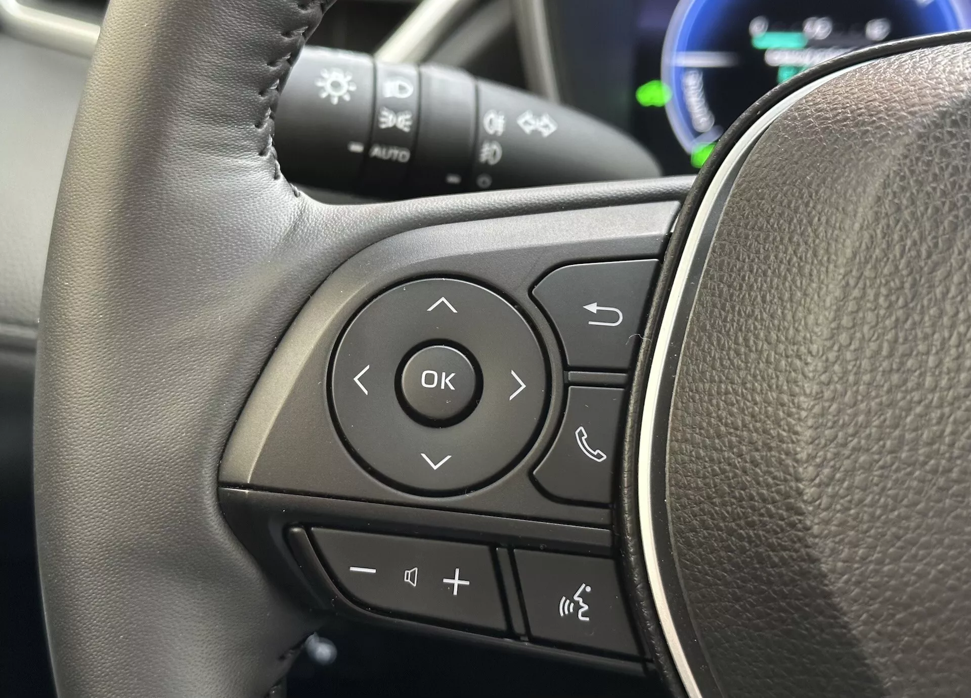 Vue détaillée du volant de la Toyota Corolla Cross 2022 se concentrant sur les commandes multifonctions sur le rayon gauche avec une texture semblable à celle du cuir et des boutons clairement marqués pour l'audio, la connectivité téléphonique Bluetooth, les commandes vocales et la navigation via le système d'information du conducteur