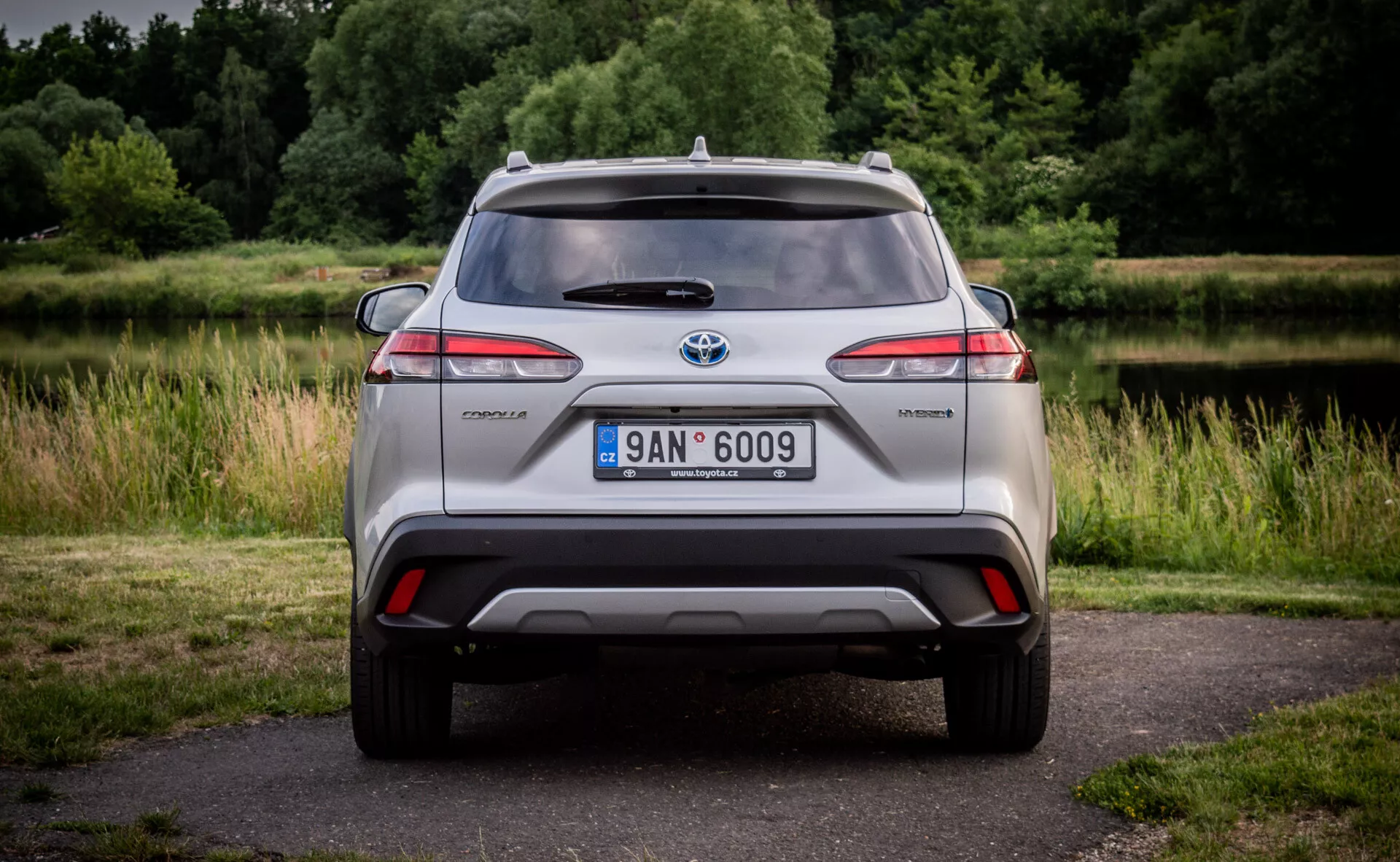 Vue arrière d'un modèle hybride Toyota C-HR mettant en avant des feux arrières LED, pare-chocs avec diffuseur intégré et réflecteurs, antenne sur le toit et jantes alliage, sur un fond naturel