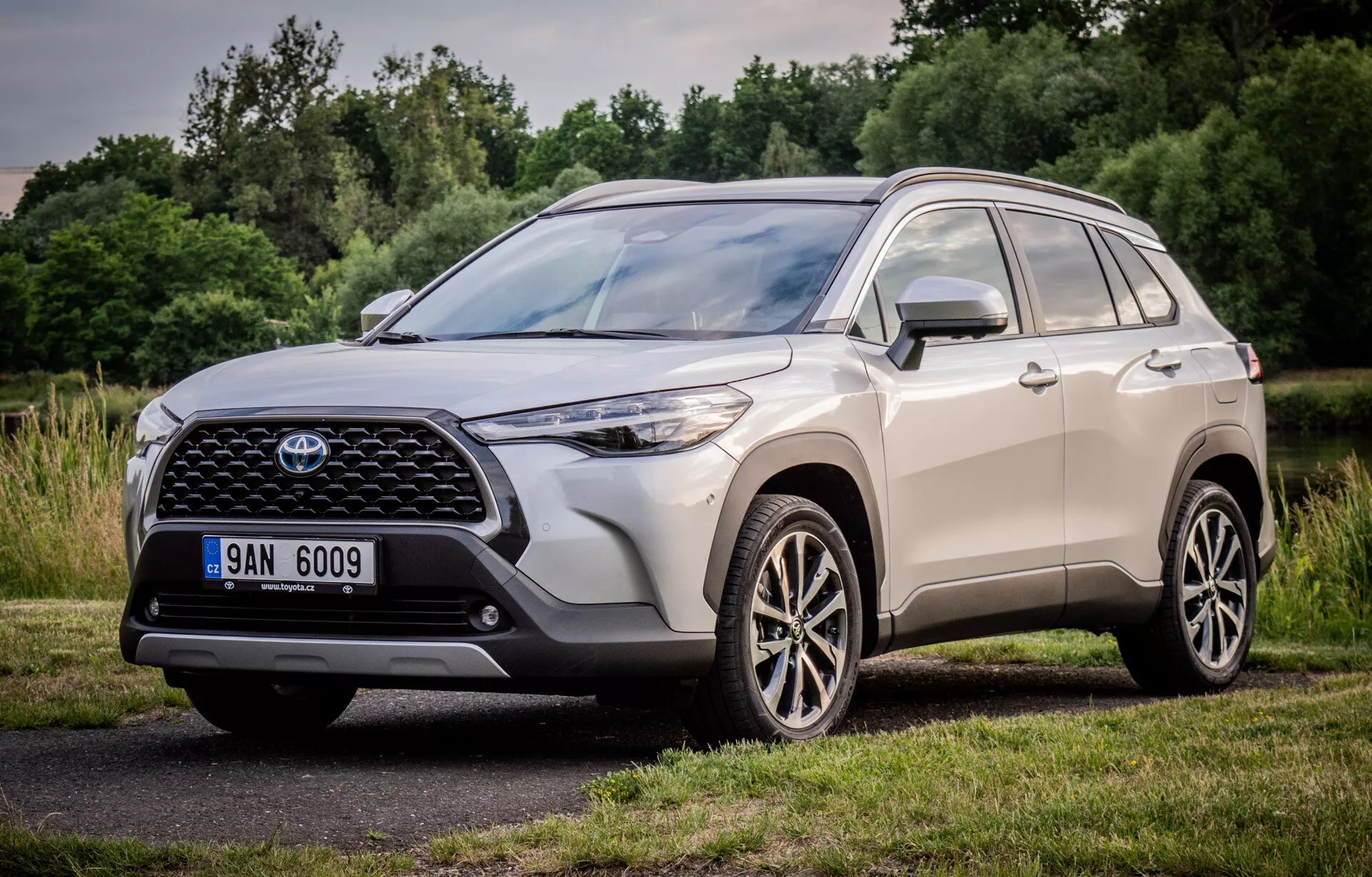 Toyota Corolla Cross 2022 présentant son design dynamique avec une vue en perspective frontale et latérale trois quarts, mettant en avant la grande grille frontale à motif, les unités de phares LED élégants et les roues en alliage à multiples branches, garée dans un cadre naturel
