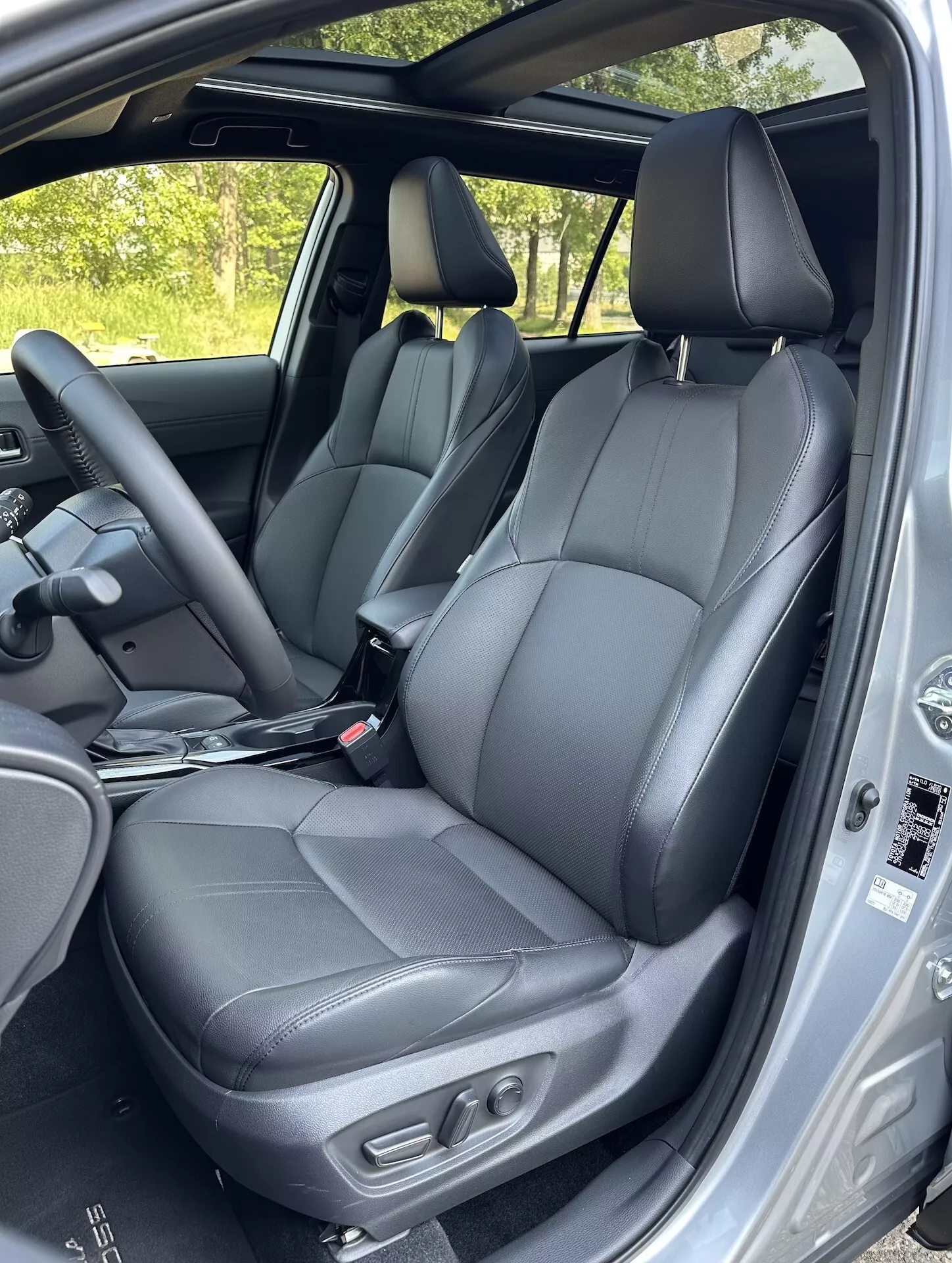 Vue intérieure de la Toyota Corolla Cross 2022 mettant en évidence les sièges avant en cuir noir avec commandes de réglage, une partie des sièges arrière, le volant et les caractéristiques de sécurité du cadre de porte à la lumière naturelle du jour