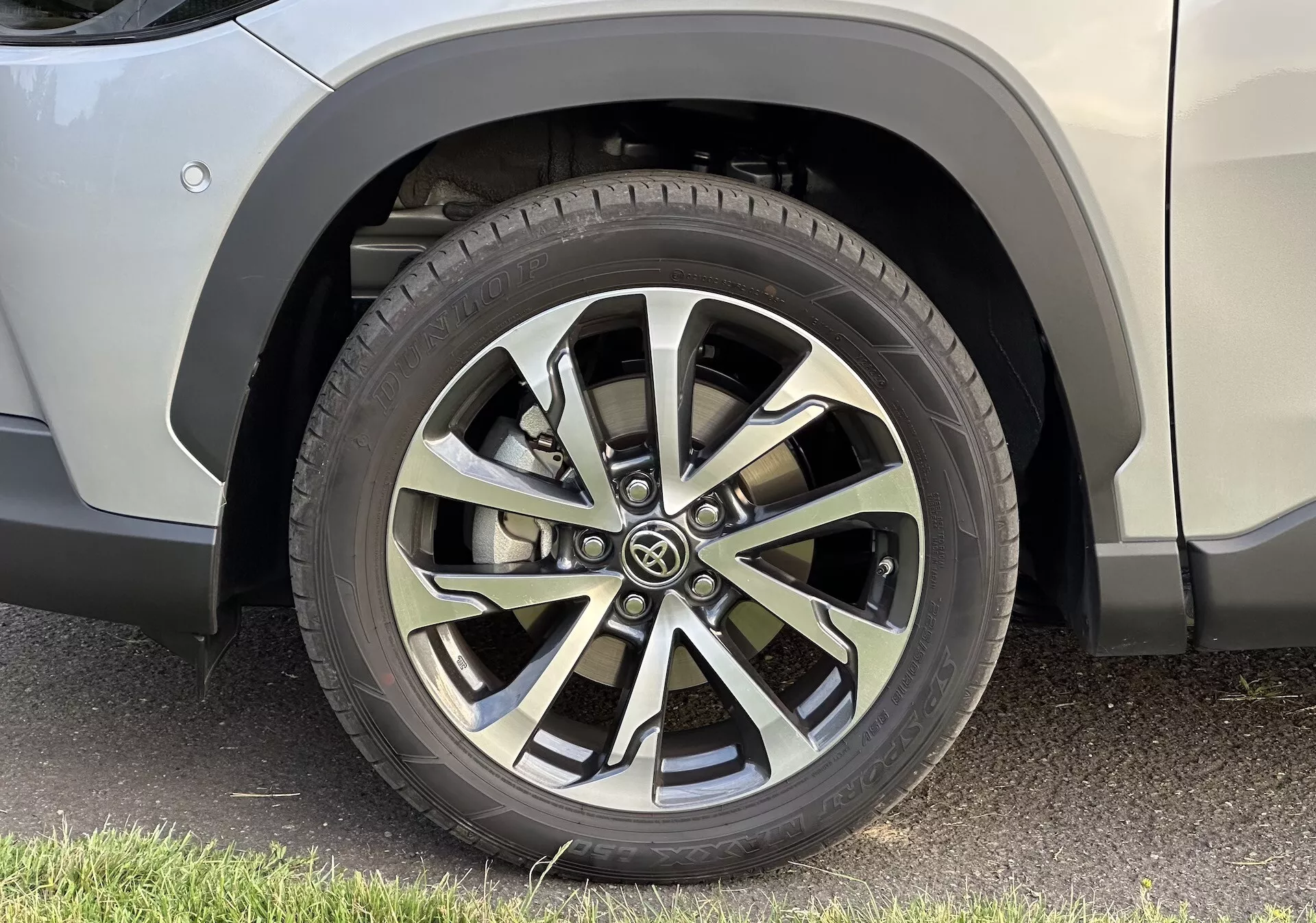 Gros plan détaillé sur la roue avant droite du Toyota Corolla Cross 2022 avec conception de jante en alliage à multiples branches, motif de bande de roulement de pneu toutes saisons et carrosserie de SUV impeccable, stationnée sur l'asphalte.