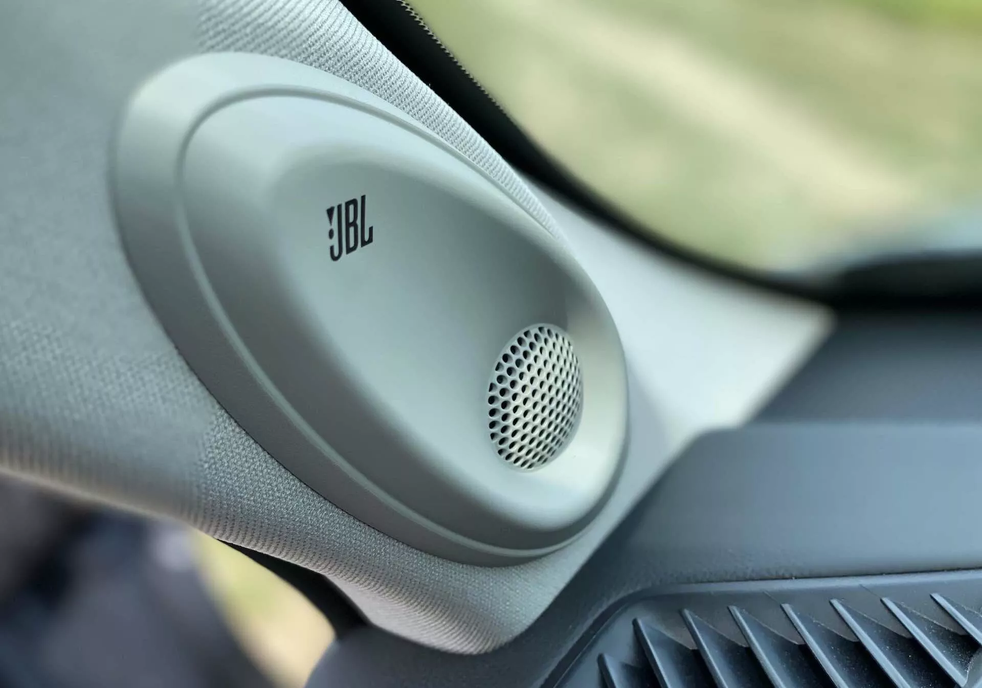 Vue rapprochée de l'intérieur du Toyota Highlander 2.5 Hybrid Business Edition 2021, mettant en avant un haut-parleur monté sur la porte JBL avec une grille circulaire en maille et un boîtier texturé, mettant en valeur l’audio de voiture premium et les caractéristiques des véhicules de luxe.