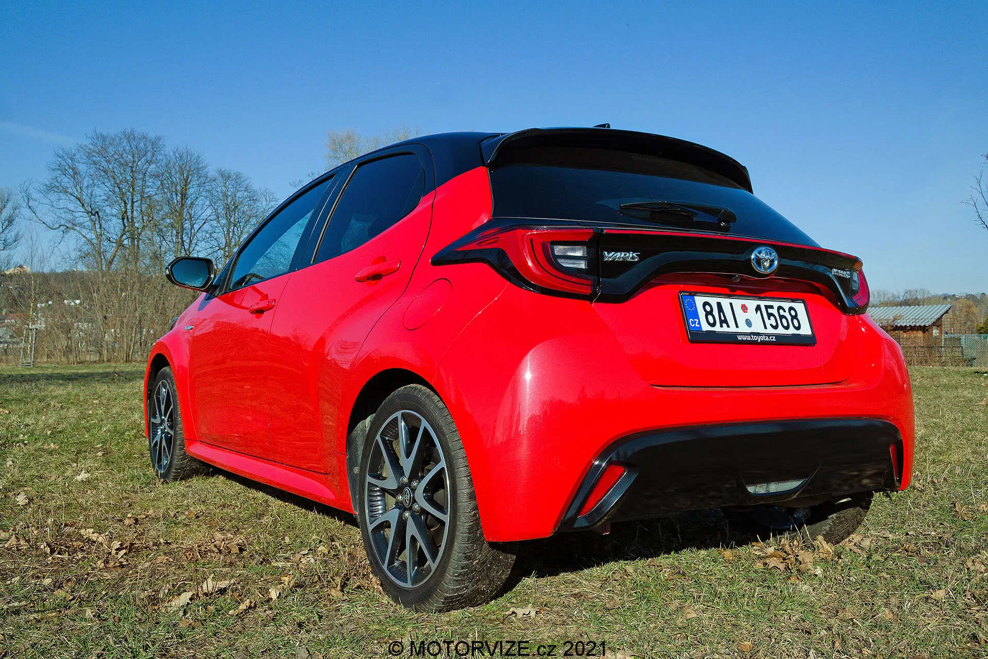 Vue arrière trois quarts d'une Toyota Yaris 2020 rouge vif, vue sous un angle bas, mettant en valeur les lignes de design et les caractéristiques clés comme les feux arrière à LED, le spoiler arrière, l'antenne en aileron de requin et les roues en alliage à plusieurs rayons avec une finition sombre. La photo capture le détail de l'arrière et une partie du profil latéral à la lumière naturelle, mettant en avant son esthétique sportive et ses éléments modernes.