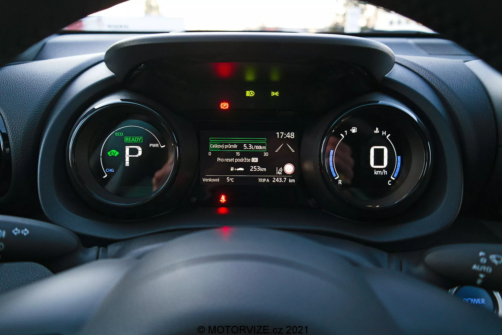 Vue intérieure du tableau de bord de la Toyota Yaris 2020 centrée sur le bloc d'instruments, prise du point de vue du conducteur montrant des jauges numériques, des indicateurs de véhicule électrique ou hybride, et un écran multi-informations avec des fonctionnalités telles que la distance du trajet, la température extérieure et l'autonomie de la batterie.