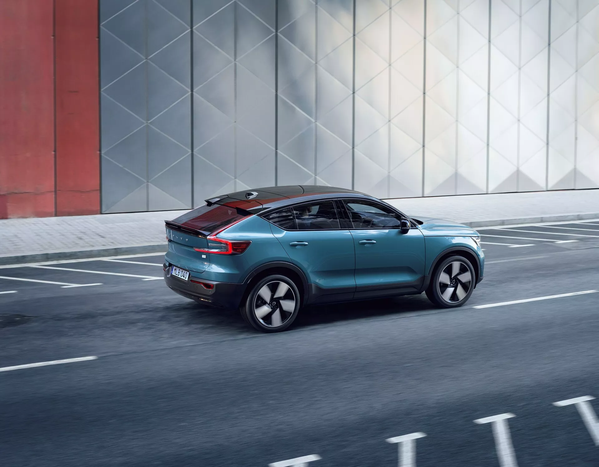 Vue trois quarts arrière dynamique de la Volvo C40 2021, mettant en valeur son design élégant, ses éléments aérodynamiques, ses feux arrière modernes, ses roues personnalisées et son toit panoramique, se déplaçant sur une route urbaine.
