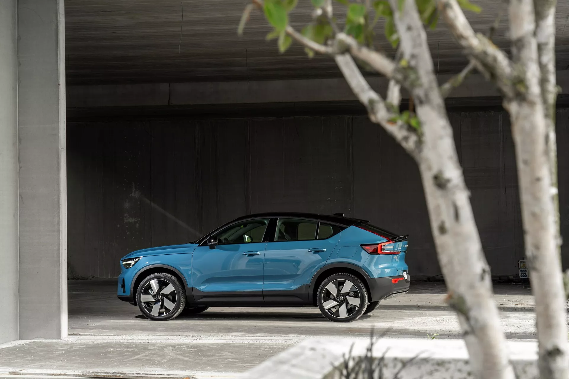 Profil latéral d'une Volvo C40 2021 bleu vif garée dans un espace spacieux, montrant son design moderne et élégant, des roues en alliage argentées à plusieurs rayons, des vitres légèrement teintées et une éventuelle trappe de port de charge.