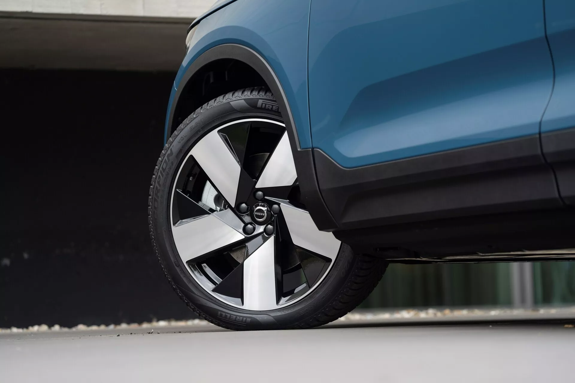 Vue en gros plan sous un angle bas d'une Volvo C40 2021 (1ère génération) moderne, se concentrant sur la roue avant et la carrosserie latérale adjacente. La jante multibrins présente une combinaison de finitions métalliques et sombres, complétée par un pneu à profil bas. La carrosserie aérodynamique du véhicule bleu foncé met en évidence des lignes épurées et des éléments de design sophistiqués.