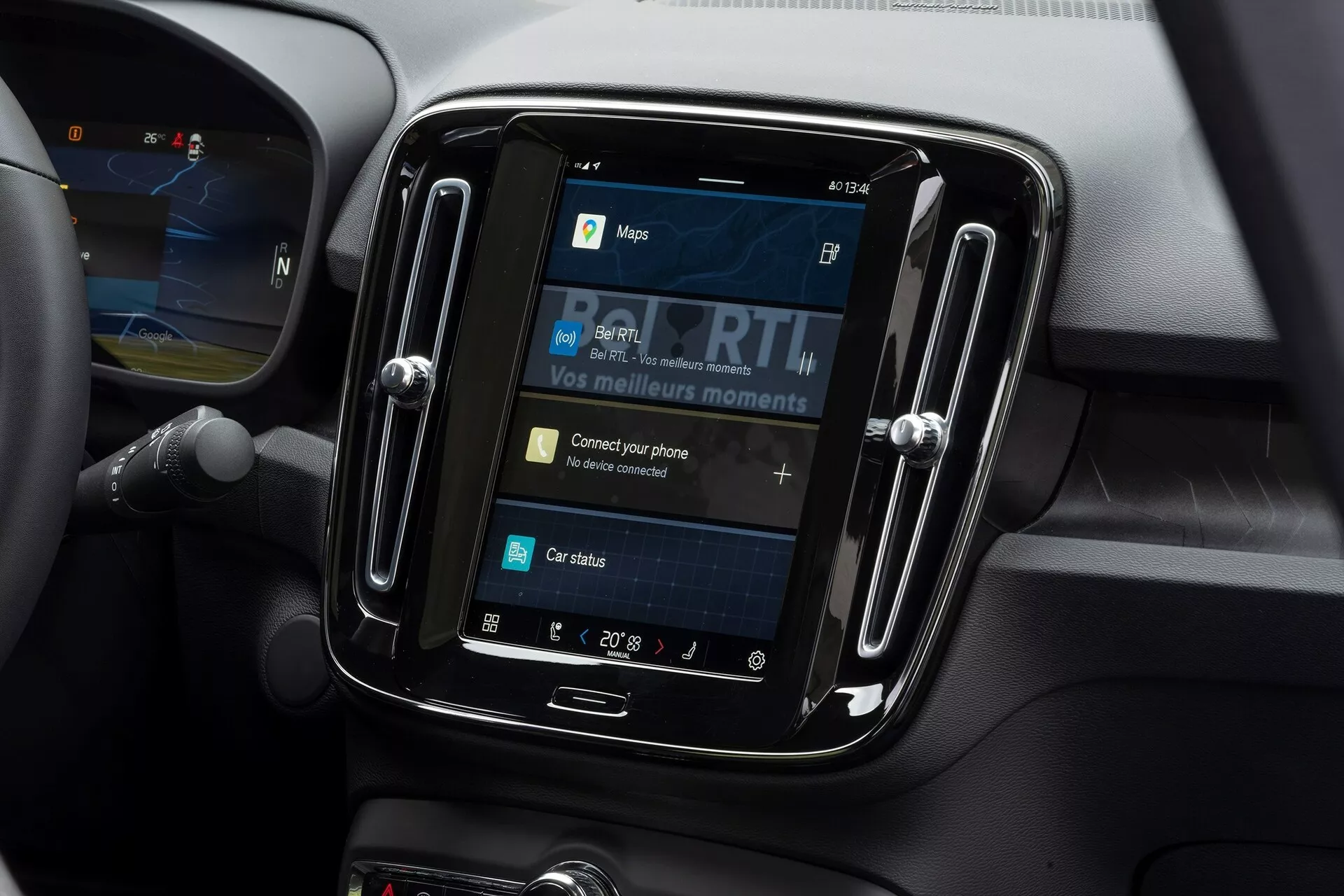 Vue rapprochée du système d'infodivertissement à l'intérieur d'une Volvo C40 2021. La prise de vue, réalisée sous un angle légèrement abaissé, se concentre sur l'écran tactile encadré d'une bordure noire brillante. L'écran affiche des options telles que cartes, médias, connectivité téléphonique et état de la voiture, avec 'Connectez votre téléphone' comme élément interactif. Autour du système d'infodivertissement, on trouve des matériaux doux au toucher et des lignes de contour indiquant des évents d'air, faisant référence à un intérieur de voiture moderne. Le réglage de la température montre 20° Celsius et une partie du volant est visible à gauche.