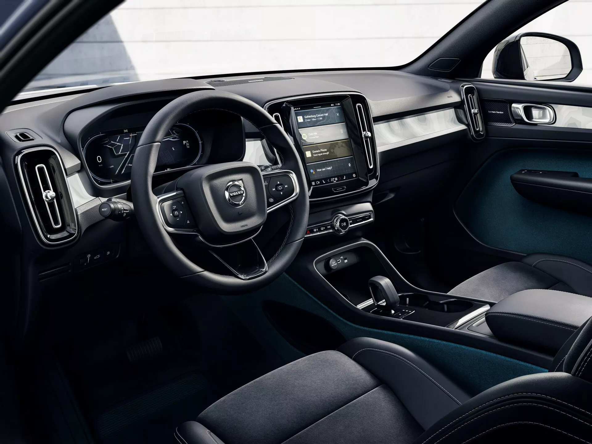Photo intérieure d'une Volvo C40 2021 (1ère génération) prise de l'extérieur, montrant le poste de conduite avec le volant, le tableau de bord numérique, la console centrale avec le système d'infodivertissement tactile, les commandes de climatisation, les sièges ergonomiques en tissu foncé, les boutons de commande de porte et un schéma de couleurs bicolore avec des éléments de design modernes et fonctionnels.