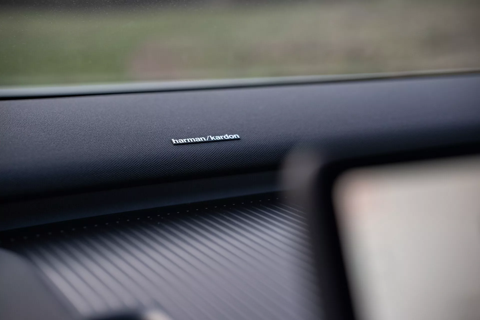 Photo de l'intérieur d'une Volvo EX30 2024 mettant en avant la marque du système audio Harman/Kardon sur le tableau de bord côté passager, démontrant la qualité élevée du matériel et accentuant la technologie supérieure du système sonore.