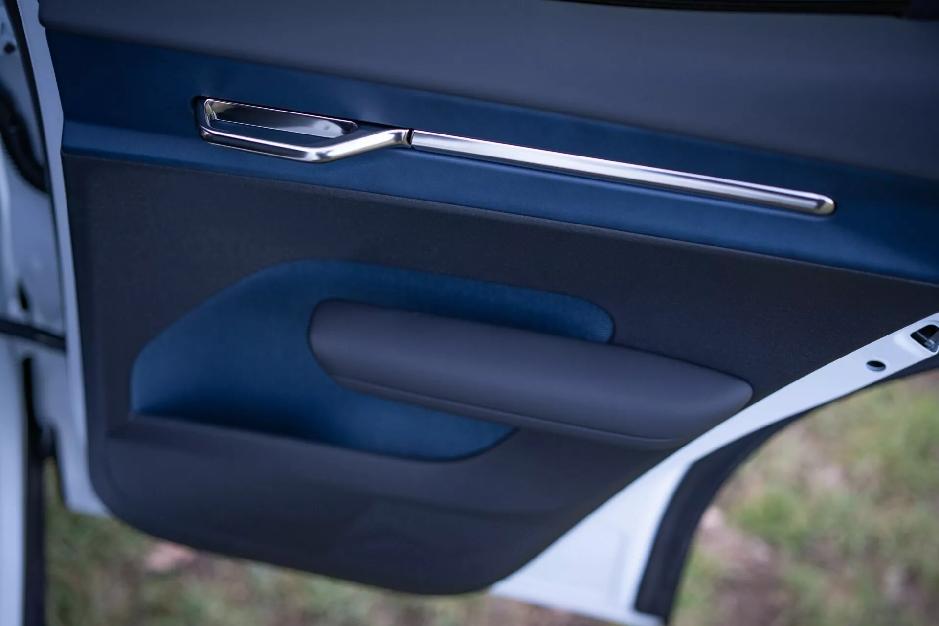 Gros plan sur l'intérieur de la porte de la Volvo EX30 2024, montrant la poignée de porte métallique élégante, l'accoudoir ergonomique et le rangement dans une finition sombre de haute qualité