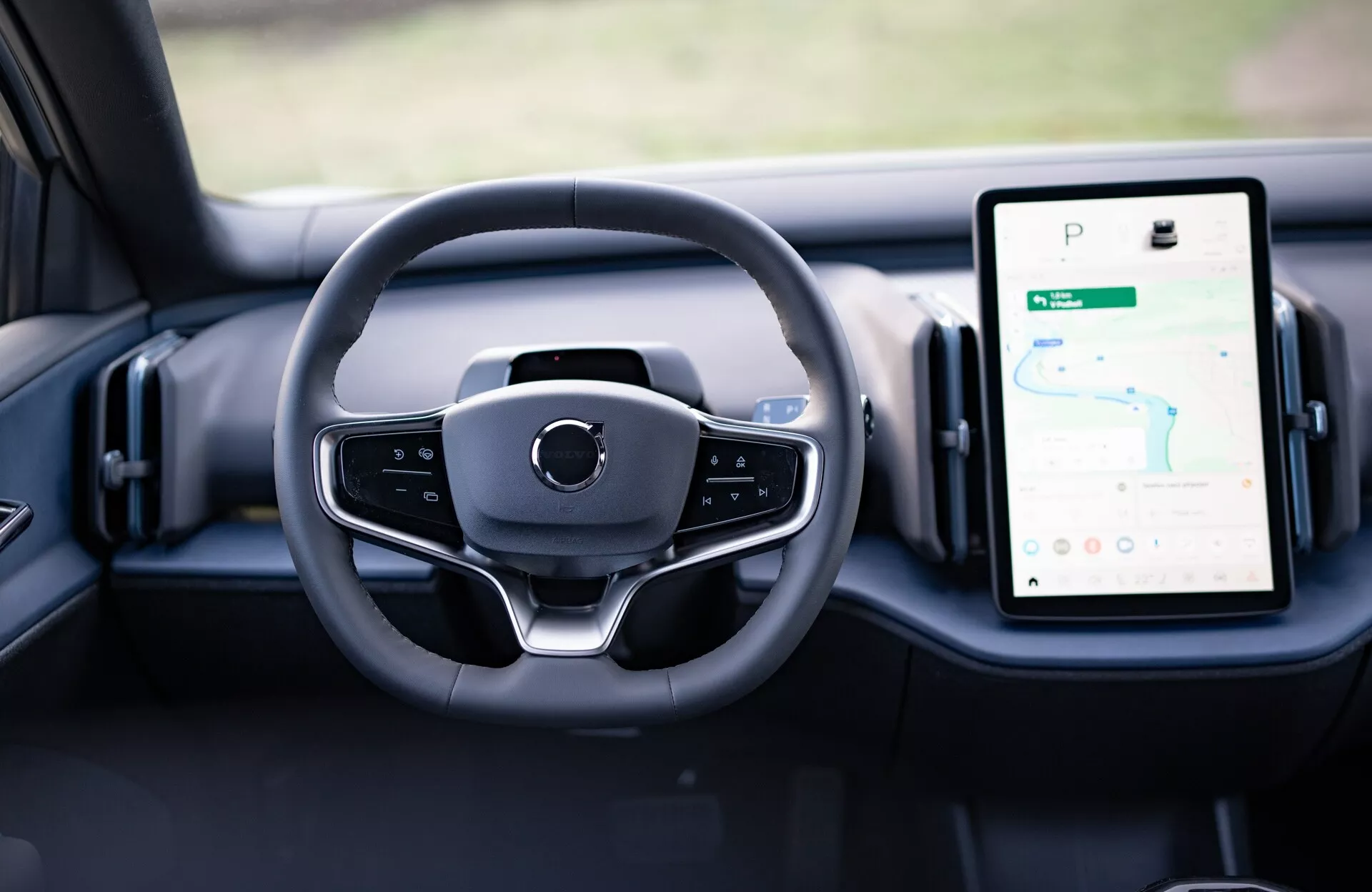 Vue intérieure du Volvo EX30 2024 montrant la conception moderne du volant et les cadrans numériques sur le tableau de bord, y compris le système d'infodivertissement tactile vertical doté de GPS.