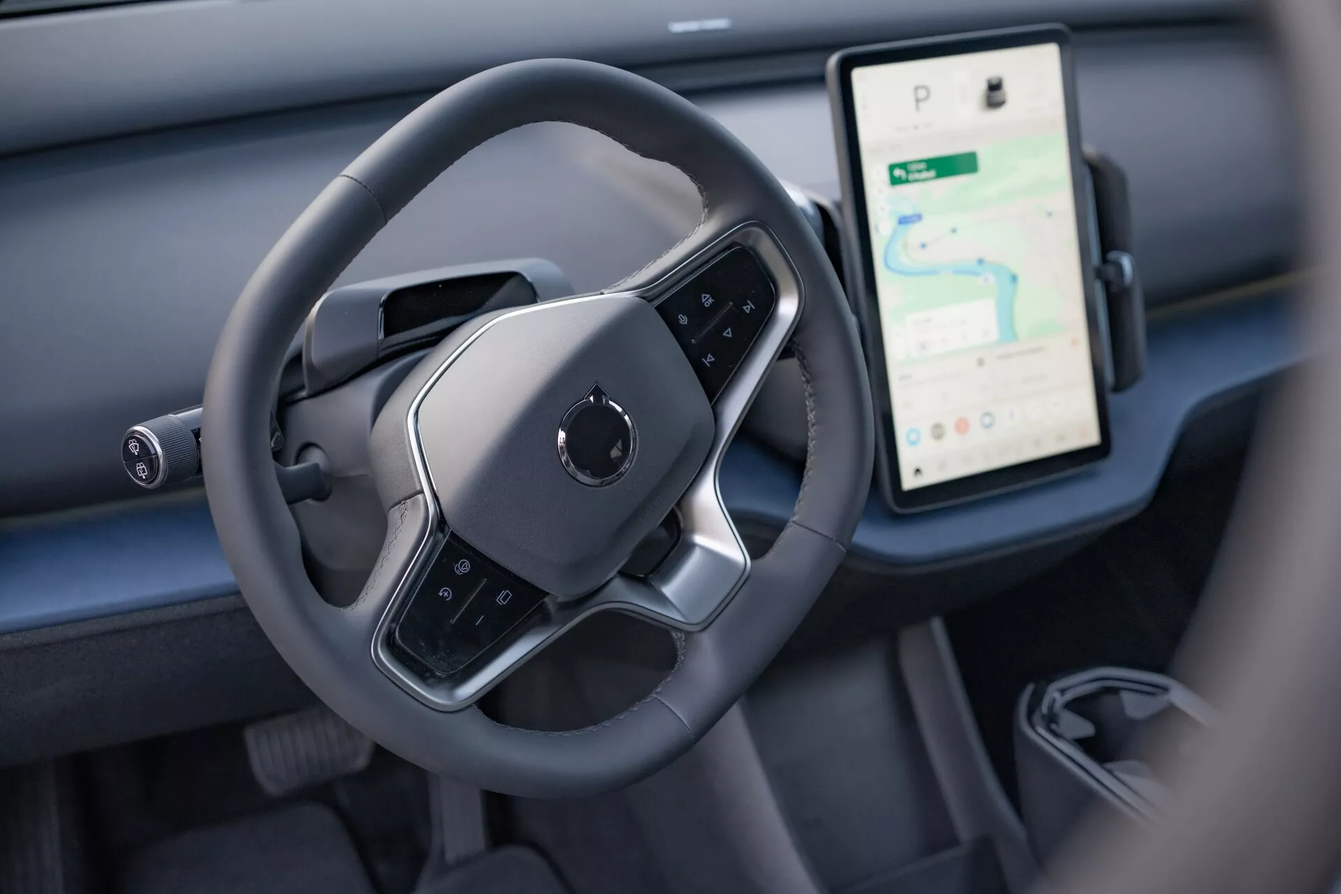 Vue intérieure du Volvo EX30 2024 mettant en évidence la zone de contrôle du conducteur avec un volant moderne à fond plat et un grand écran tactile vertical pour la navigation et les médias sur le tableau de bord