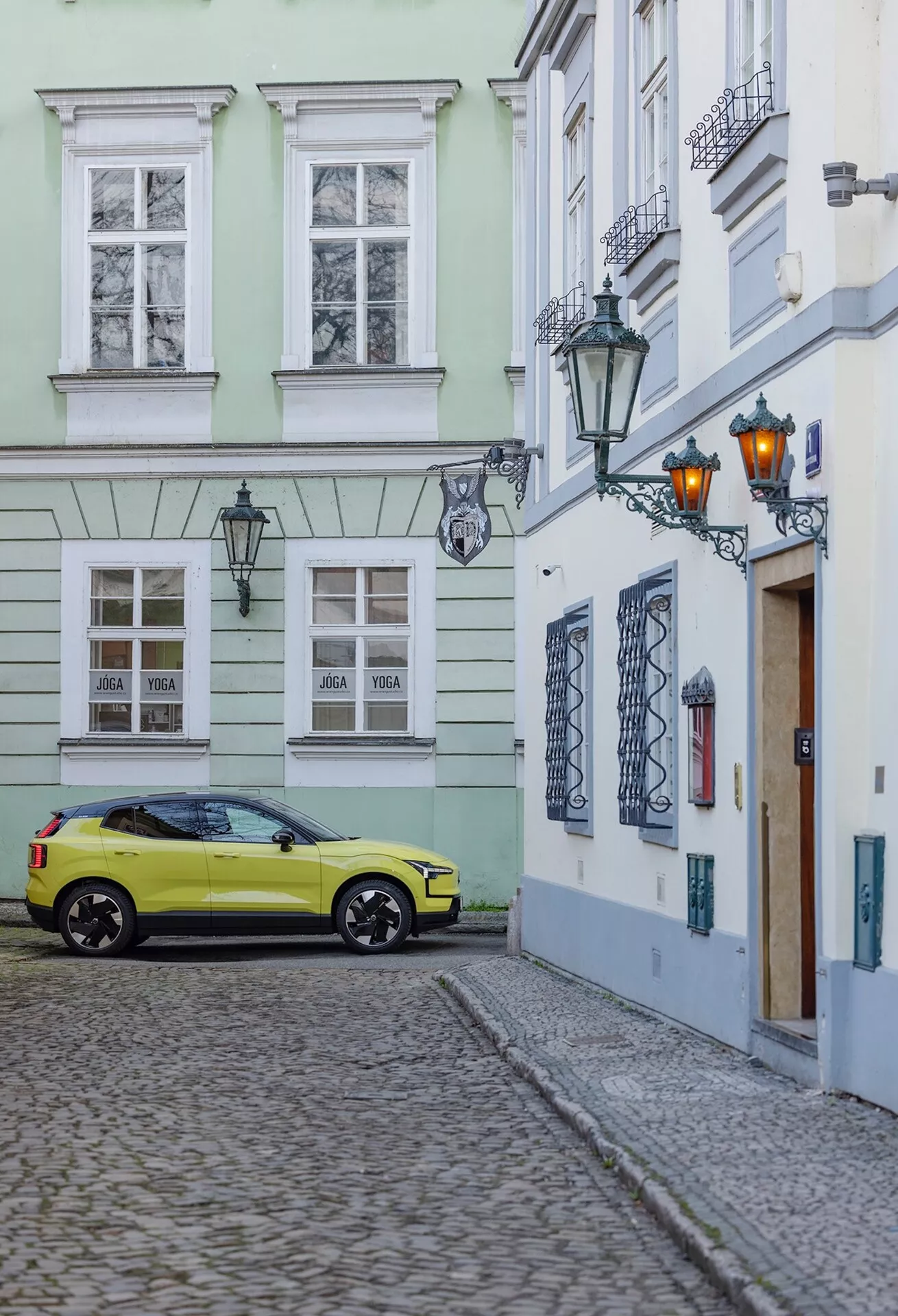 Volvo EX30 2024 garée sur une rue pavée dans un cadre de vieille ville, capturée depuis un angle arrière de trois quarts montrant le côté droit et l'arrière de la voiture incluant les roues, les feux arrière et les détails partiels du toit en couleur jaune vif