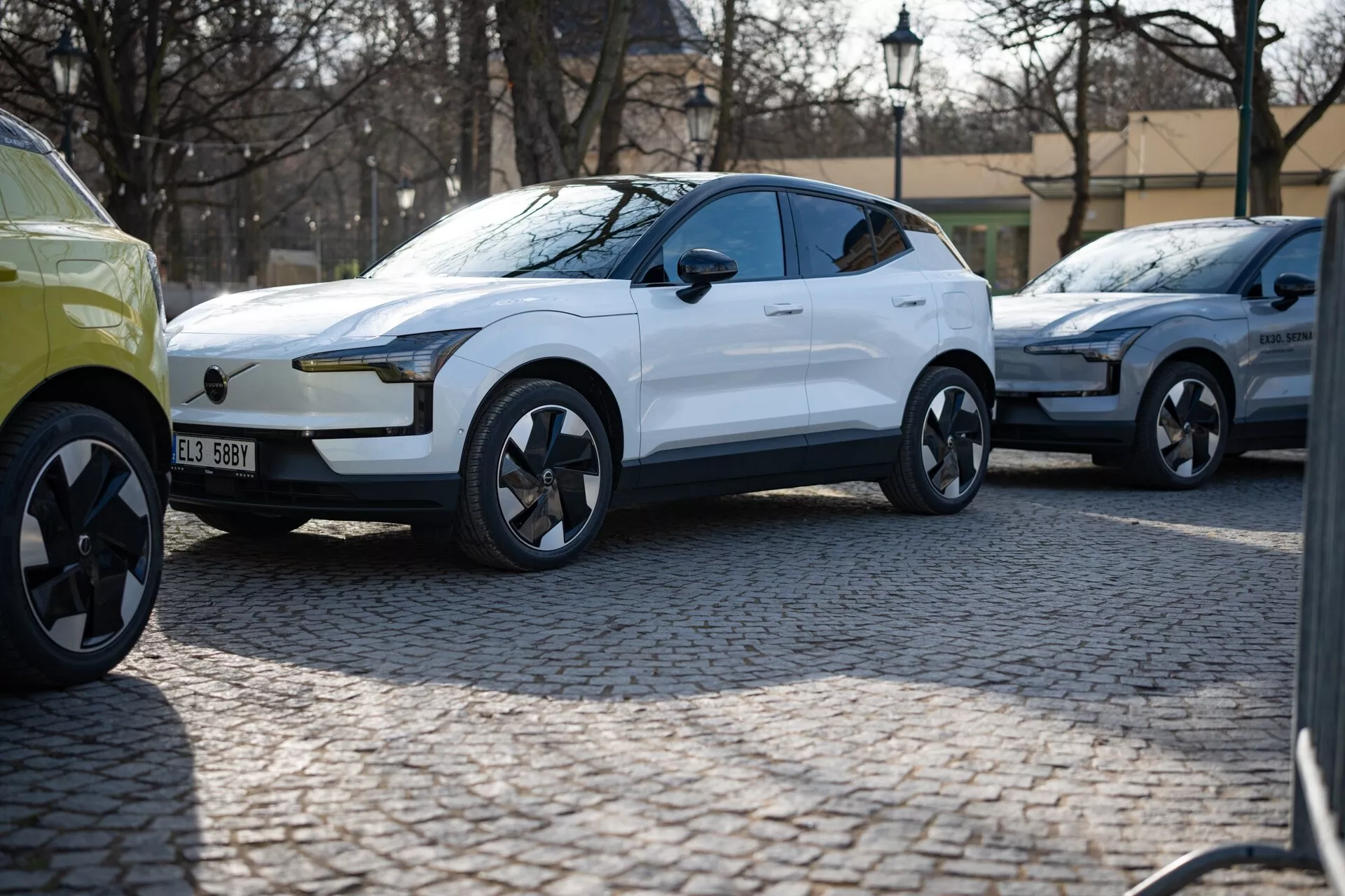 SUV crossover moderne blanc de 2024 en vue trois quarts stationné sur une rue pavée, avec une peinture brillante, des feux diurnes à LED, des poignées de porte affleurantes et des roues en alliage au design dynamique suggérant luxe et performance, probablement un véhicule électrique.