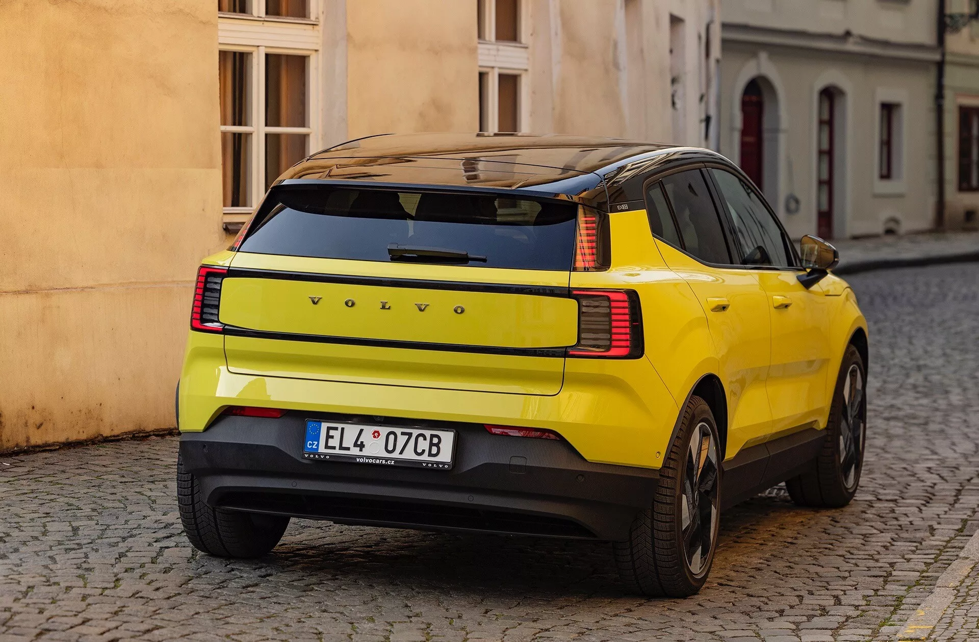 SUV jaune Volvo EX30 2024 affichant sa courbure distincte du panneau arrière, ses feux arrière LED et ses caractéristiques de sécurité, garé dans une rue pavée vue de trois quarts arrière