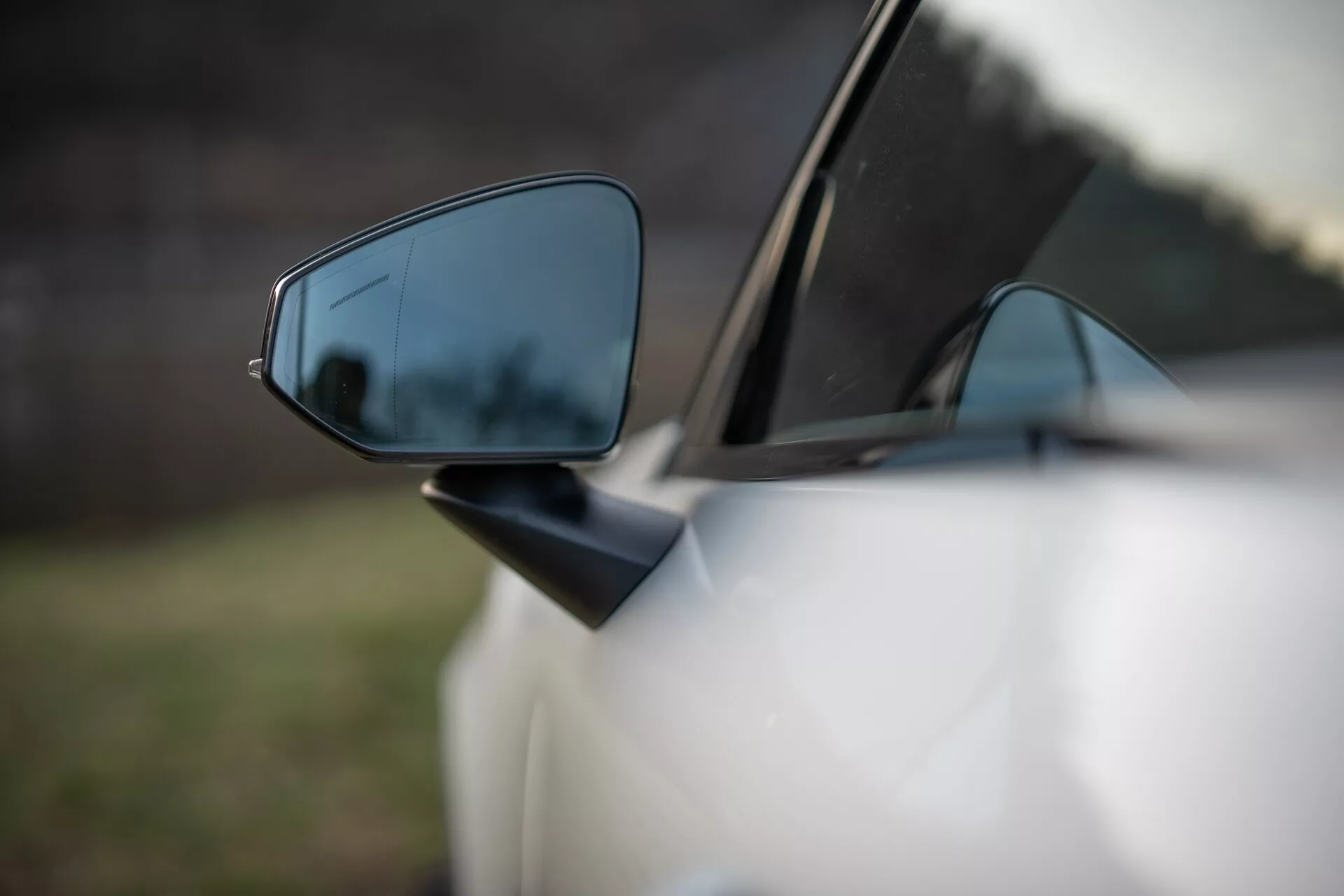 Gros plan sur le rétroviseur côté conducteur de la Volvo EX30 2024 démontrant des fonctionnalités de sécurité avancées et un design aérodynamique, avec une profondeur de champ réduite mettant en valeur le miroir contre un arrière-plan flou.