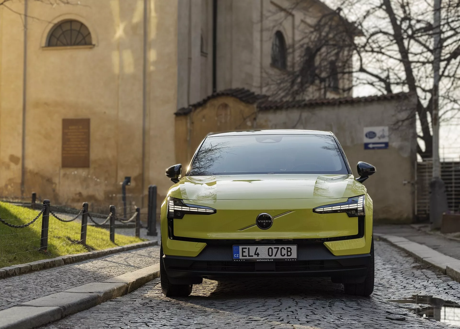 Voiture électrique moderne Volvo EX30 2024 en chartreuse, garée dans une rue pavée, vue d'une perspective avant-droite avec des phares LED et un design aérodynamique du capot souligné contre un fond européen historique.