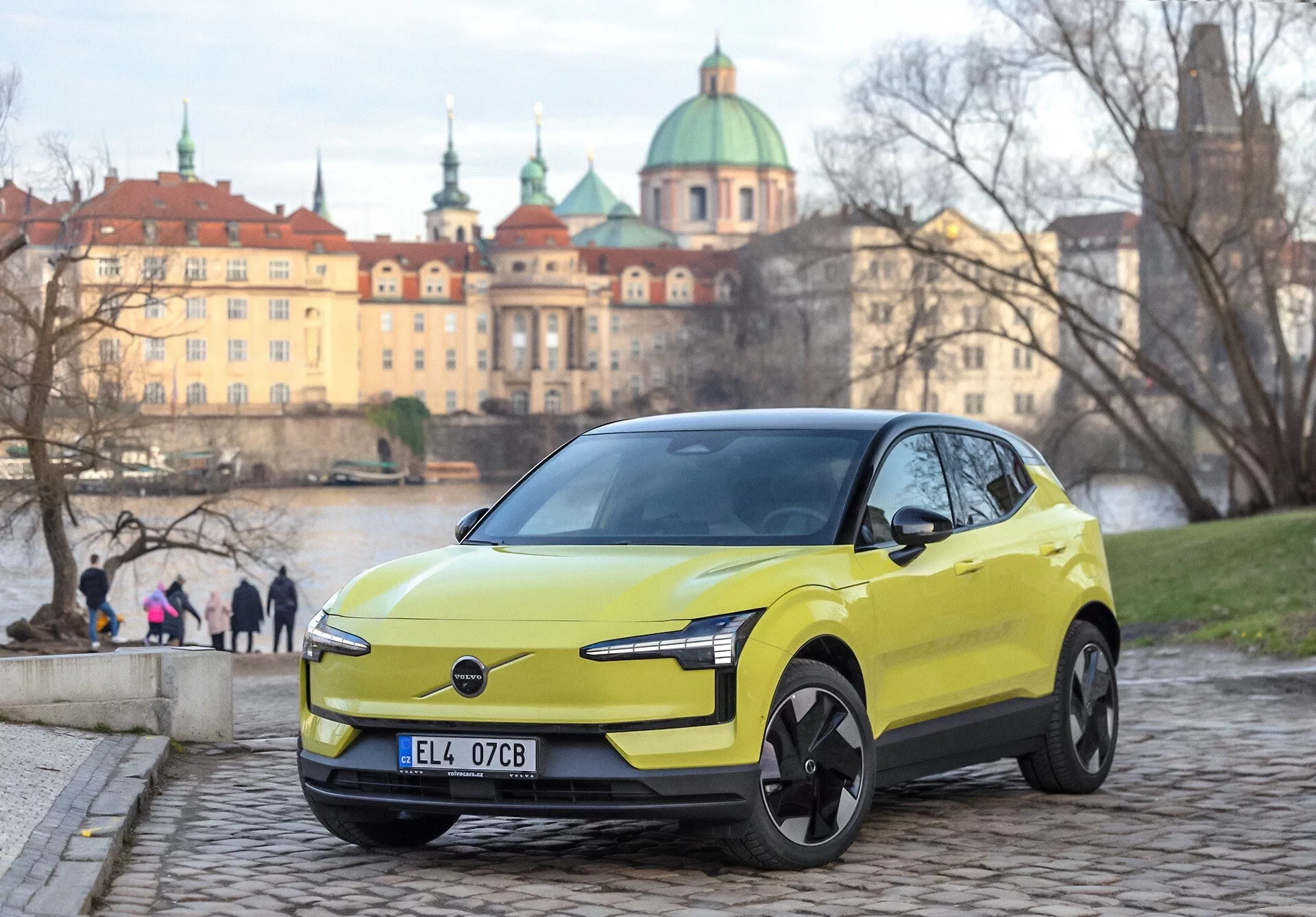 Volvo EX30 2024 en vert lime, vue avant trois-quarts sur pavés, avec phares LED modernes et caractéristiques de design électrique, arrière-plan urbain européen