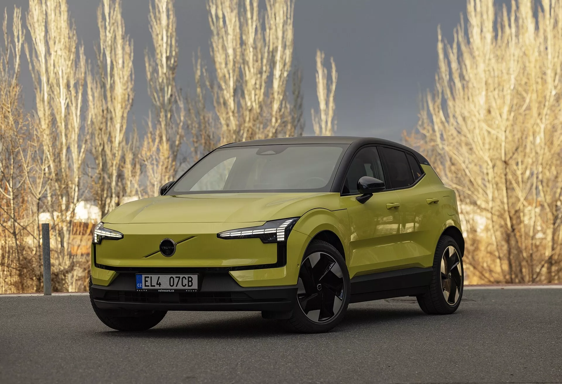 Voiture électrique Volvo EX30 2024 moderne de couleur vert lime en vue de trois quarts avant mettant en évidence ses phares LED élégants, l'absence de grille traditionnelle pour améliorer l'aérodynamique, de grandes roues en alliage noir, des rétroviseurs extérieurs de couleur carrosserie avec technologie intégrée potentielle, un profil latéral lisse et aérodynamique avec une apparence de coupé, et une finition métallique vibrante, stationnée dans un cadre naturel