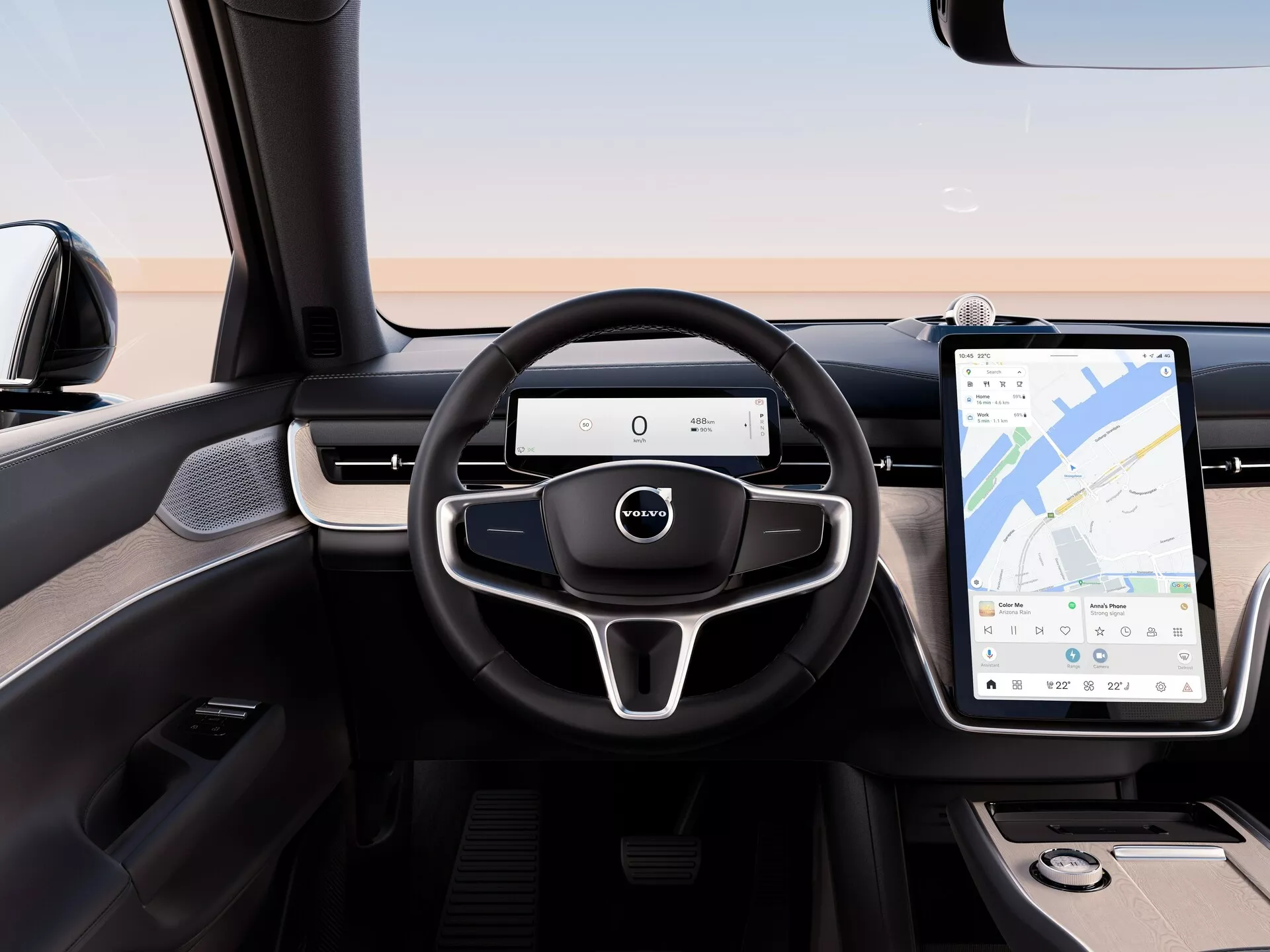 Vue intérieure du Volvo EX90 2023 depuis le siège arrière, mettant en évidence le volant moderne à trois branches avec commandes multifonctions, le tableau de bord numérique et le grand système d'infodivertissement tactile avec navigation GPS
