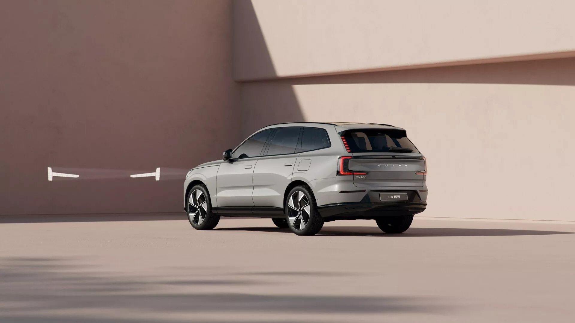 SUV Volvo EX90 2023 en perspective latérale-arrière dynamique sur fond minimaliste lisse, présentant des lignes de conception, des roues en alliage sculptées et des fonctionnalités technologiques avancées.
