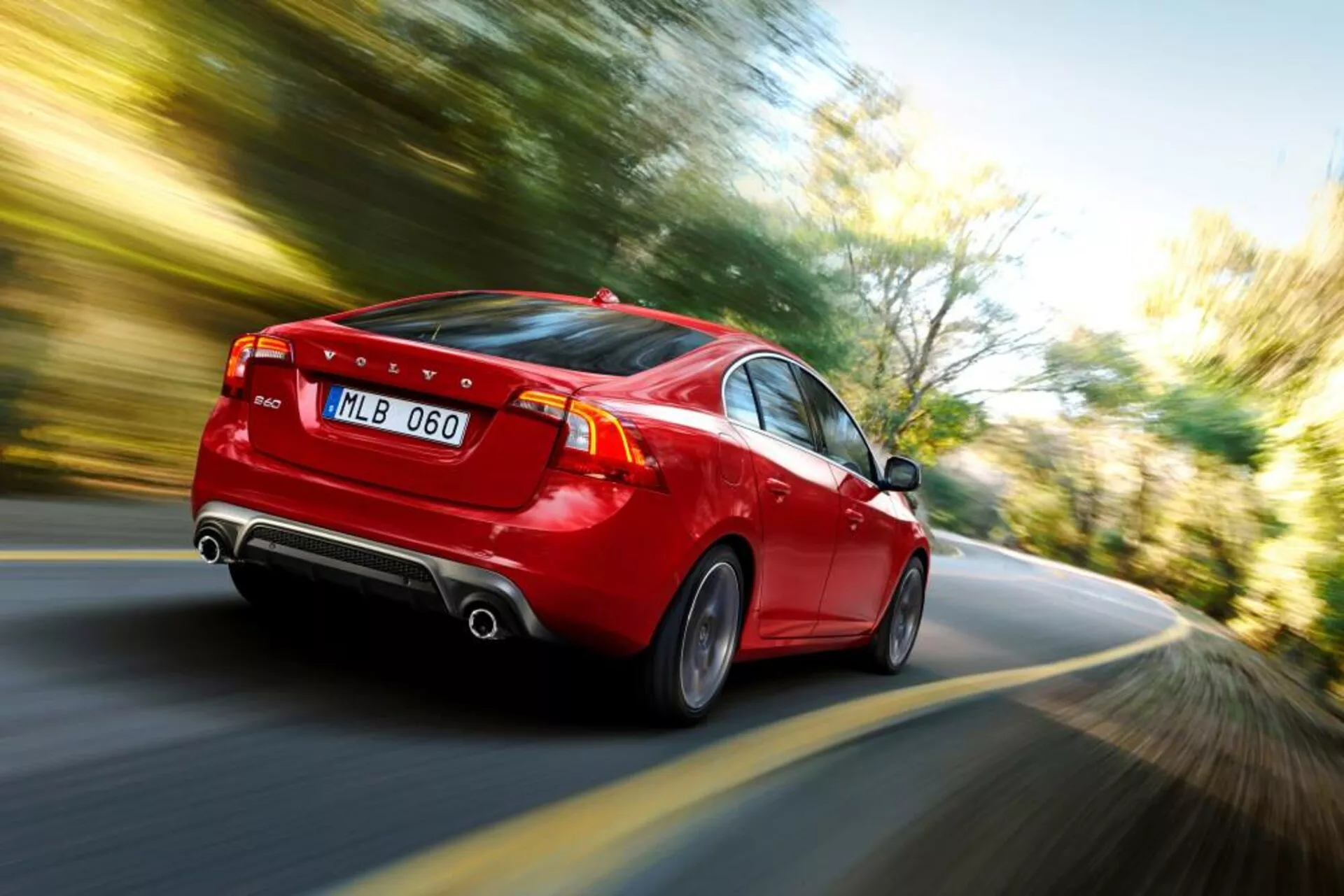 Vue arrière dynamique aux trois quarts d'une berline rouge Volvo S60-V60 2004 en mouvement, mettant en avant des feux arrière LED, double échappement, jantes en alliage élégantes et une indication claire de la vitesse grâce à l'effet de flou de mouvement.