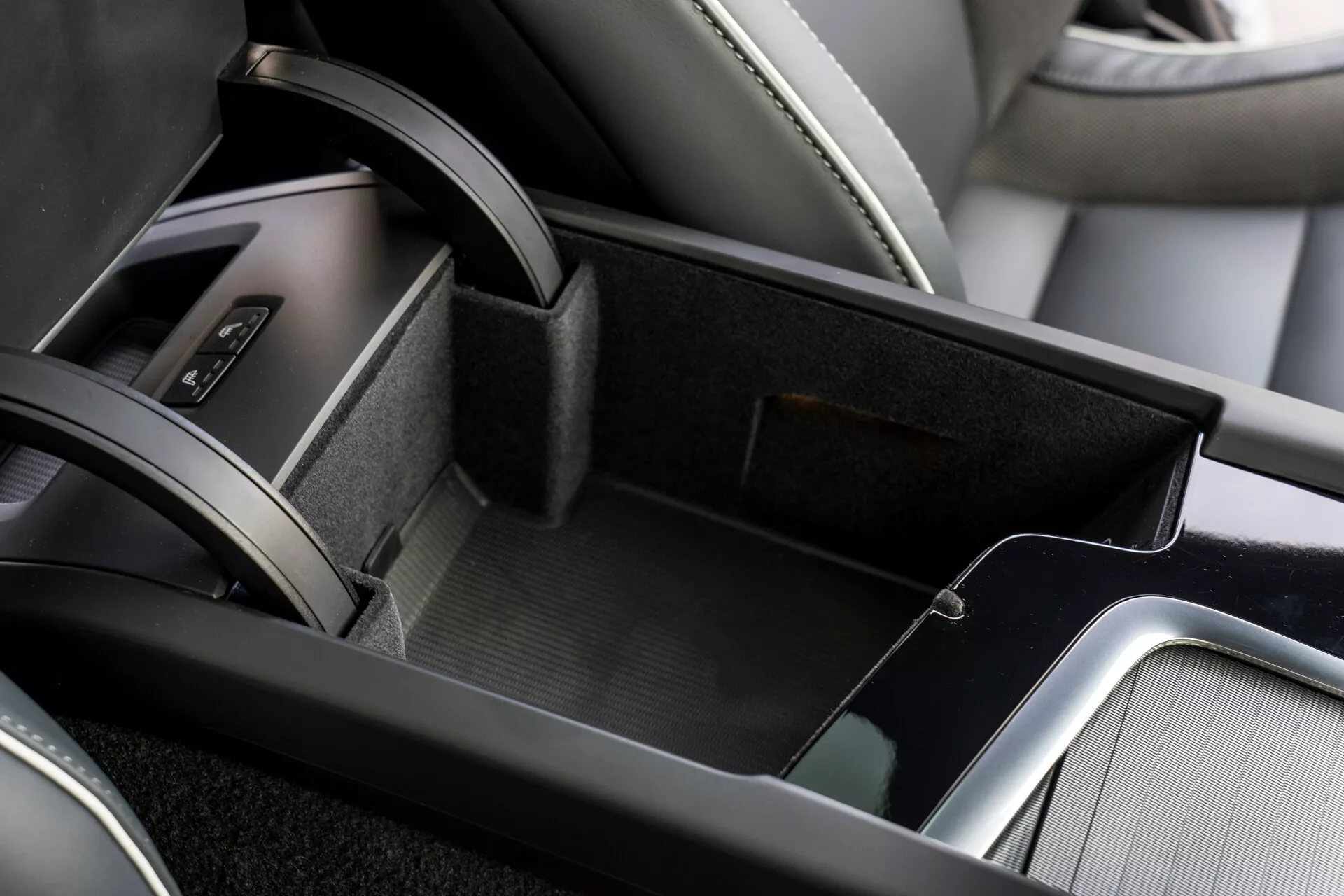 Vue rapprochée de la zone de la console centrale dans l'intérieur du Volvo XC60 2021, montrant le compartiment de rangement ouvert doublé d'un matériau semblable à du feutre, un rangement à deux niveaux avec un petit plateau supérieur, un accoudoir en cuir et des garnitures métalliques ajoutant de la sophistication. Une partie de la zone du levier de vitesse avec un soufflet en cuir est visible au bord de l'image.