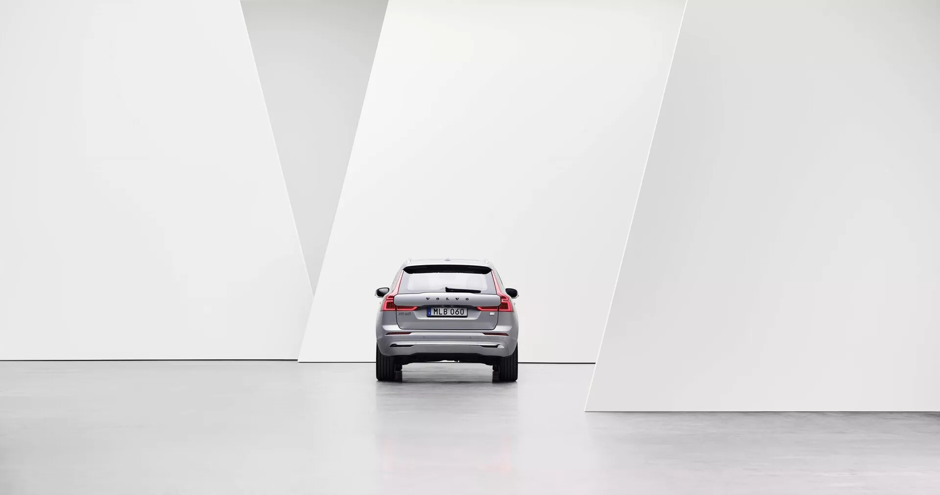 Perspective arrière centrée d'une voiture présentant des éléments de design moderne, y compris des feux arrière à LED, un pare-brise arrière, un coffre et un pare-chocs arrière dans un environnement minimaliste, lumineux et symétrique avec des sols polis et des murs blancs géométriques.