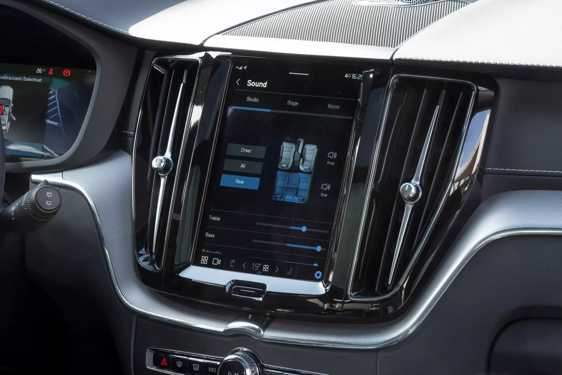 Photo de l'intérieur d'une Volvo XC60 2021 facelift, mettant l'accent sur la console centrale avec un grand système d'infodivertissement à écran tactile vertical. Prise depuis la perspective du siège passager, l'image montre également les réglages du contrôle climatique bi-zone, les grilles d'aération métalliques et les boutons de commande manuels sous l'écran, dégageant un design moderne et luxueux.