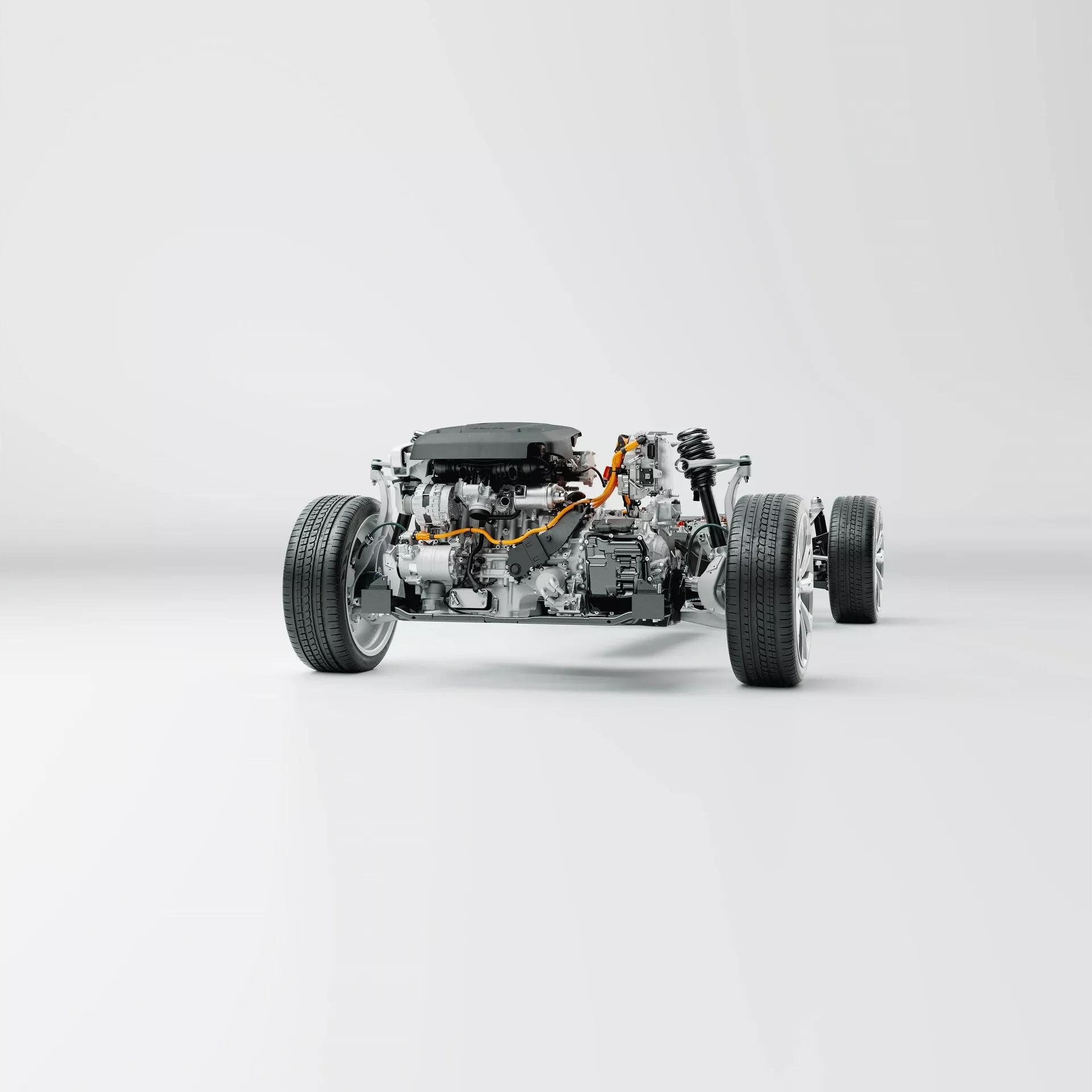 Le châssis d'une Volvo XC60 2021 de 2ème génération restylée est montré sans la carrosserie, offrant une perspective trois quarts avant. L'image offre des vues détaillées du système de suspension indépendante, des amortisseurs, des disques de frein et des étriers, du cadre du châssis, du sous-châssis, du moteur, de la transmission et des câbles orange de technologie électrique ou hybride. Photographié sur un fond blanc propre, cette image met en valeur les composants mécaniques et la symétrie du véhicule.