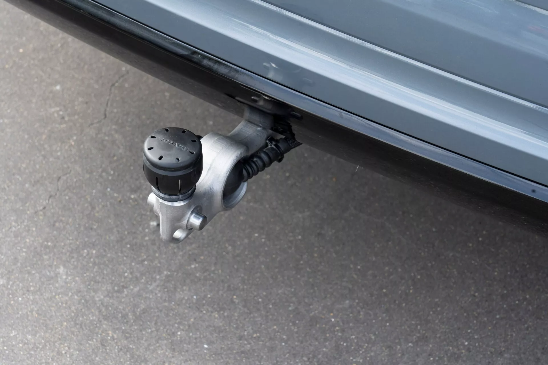 Vue rapprochée d'un marchepied latéral rétractable sur un Volvo XC60 2021 (2e génération-facelift), montrant la surface antidérapante étendue avec des points noirs surélevés sous la porte latérale du véhicule, attachée à un mécanisme de charnière métallique. Photographie prise sous un angle bas, mettant en avant la fonction automatisée conçue pour faciliter l'entrée et la sortie en réduisant la distance au sol.