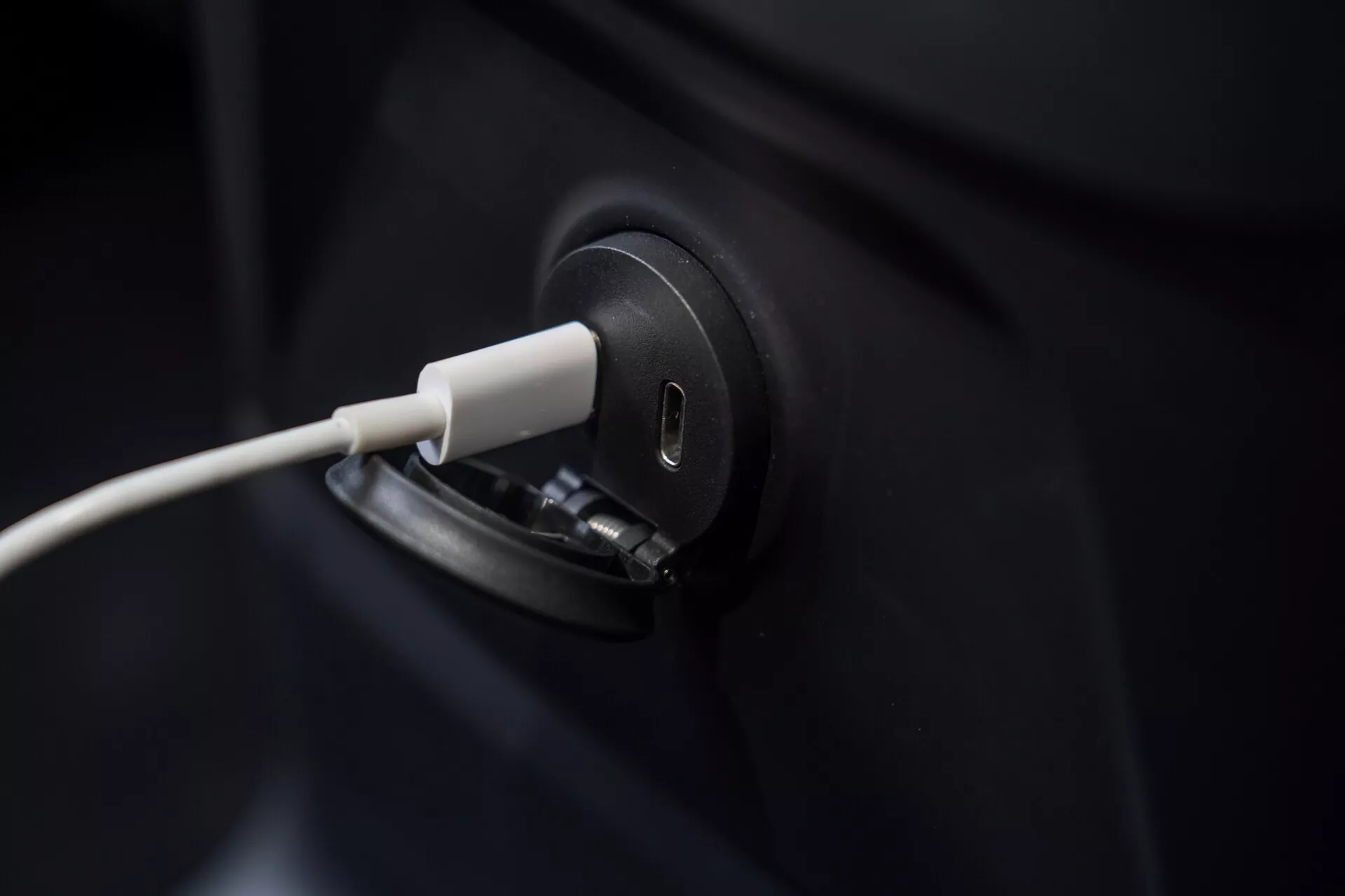 Gros plan sur la prise de charge du véhicule électrique Volvo XC60 2021 avec le câble branché, mettant en évidence le design élégant et moderne. Le cadre se concentre de près sur la prise de charge, laissant le corps sombre du véhicule en grande partie hors champ. L'arrière-plan flou souligne la précision du processus de charge des VE, symbolisant la technologie verte et le transport durable.
