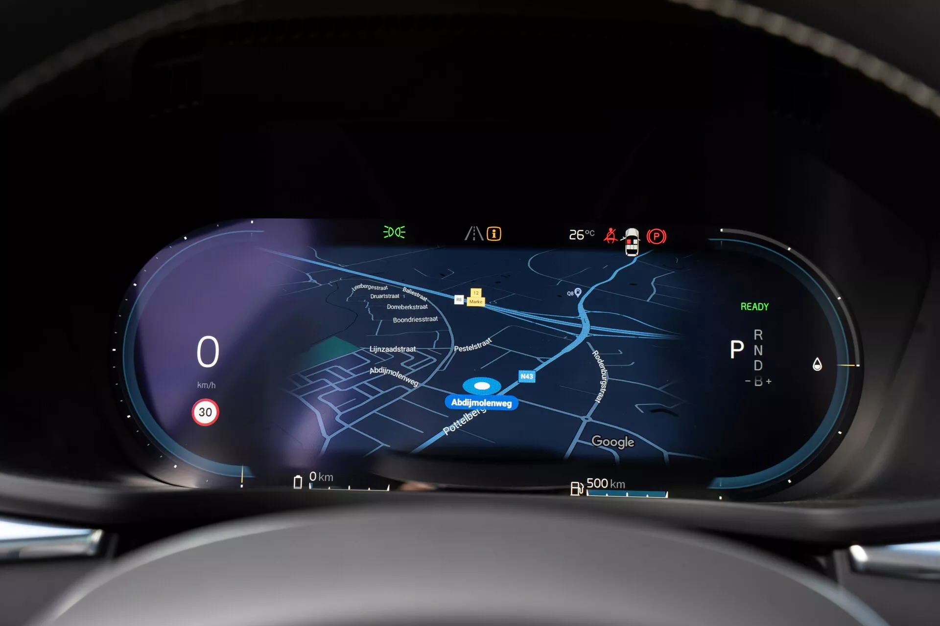 Vue intérieure de la Volvo XC60 2021 restylée de deuxième génération, présentant un tableau de bord numérique haute résolution depuis la perspective du conducteur. Le tableau de bord comporte un écran large avec un compteur de vitesse indiquant zéro, un indicateur de vitesse montrant 'P' et une carte de navigation centrale en mode nuit. Plusieurs icônes pour la réception du signal, la température extérieure, la charge de la batterie et les fonctions d'assistance au conducteur sont visibles le long du bord supérieur, indiquant une connectivité en temps réel et des capacités technologiques avancées.