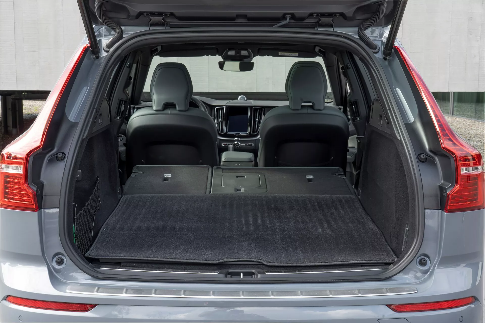 Zone de chargement arrière d'une Volvo XC60 2021 (2ème génération facelift) vue de l'arrière. L'espace du coffre ouvert révèle un plancher de chargement plat, moquetté et vide, avec les sièges arrière rabattus pour augmenter la capacité de stockage. L'intérieur est moderne, avec un tapis protecteur au sol, mais sans outils d'organisation visibles, tels qu'un filet de chargement ou des crochets.