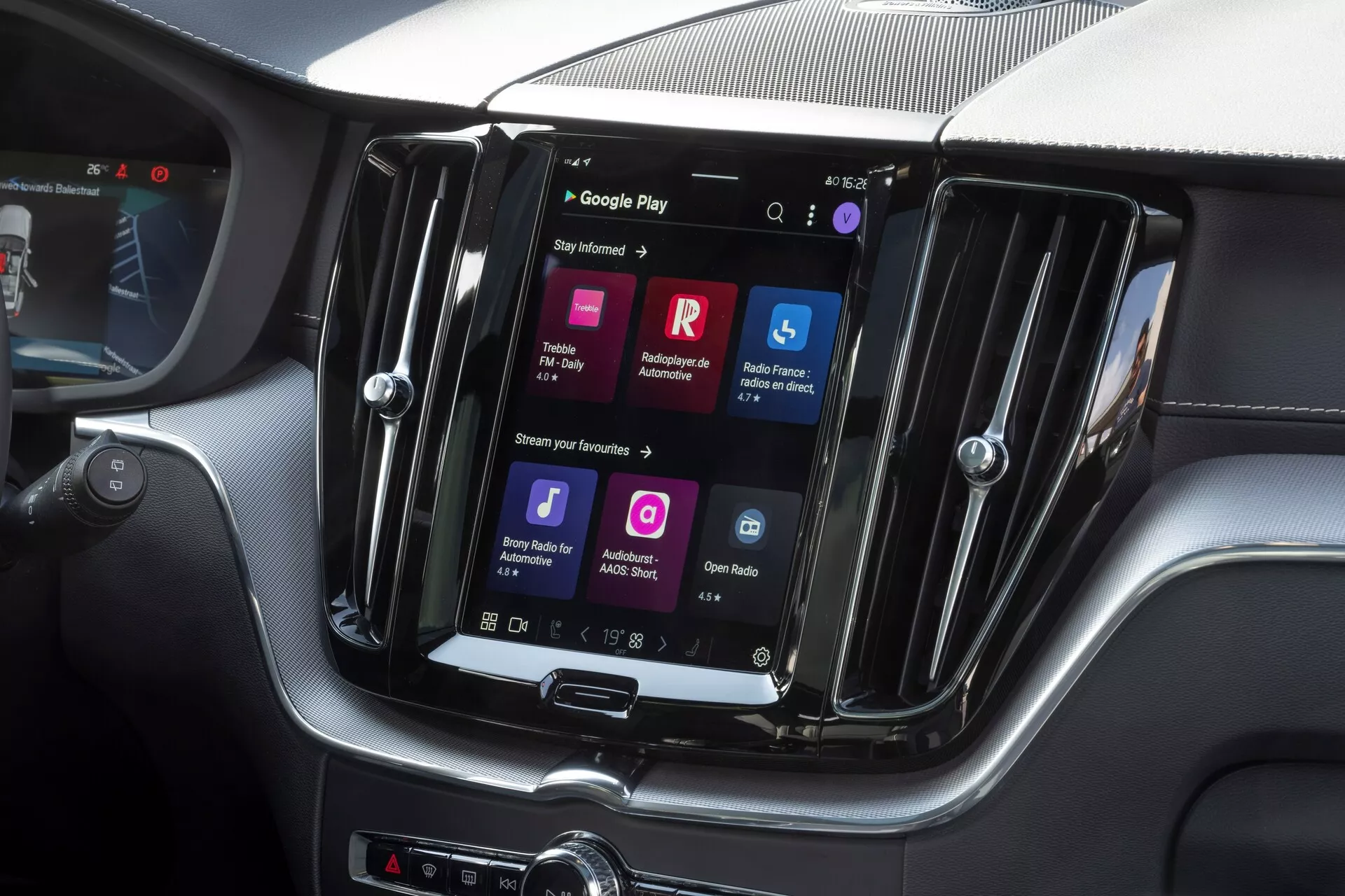 Gros plan sur la console centrale de la Volvo XC60 2021 avec un système d'infodivertissement avancé à écran tactile orienté verticalement. Écran encastré dans un cadre brillant avec finition haut de gamme et accents argentés. L'écran affiche des icônes colorées, y compris Google Play, indiquant un logiciel avancé avec connectivité des applications, reconnaissance vocale, accès à Internet et streaming multimédia. Design moderne et élégant avec textures en fibre de carbone sur le tableau de bord. Boutons physiques pour le contrôle climatique sous l'écran. Vue depuis le siège passager avant, se concentrant sur la section centrale de la console, suggérant un véhicule de luxe.