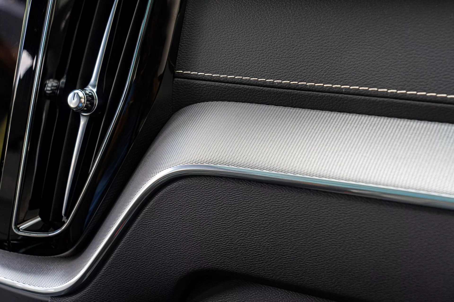Gros plan d'une section du panneau de porte intérieur d'une voiture, mettant en valeur un design moderne et élégant. Le panneau comporte une poignée de porte chromée avec une élégance minimaliste, des coutures précises sur un revêtement en cuir et un insert en métal brossé ajoutant un contraste de texture, reflétant luxe et qualité artisanale.