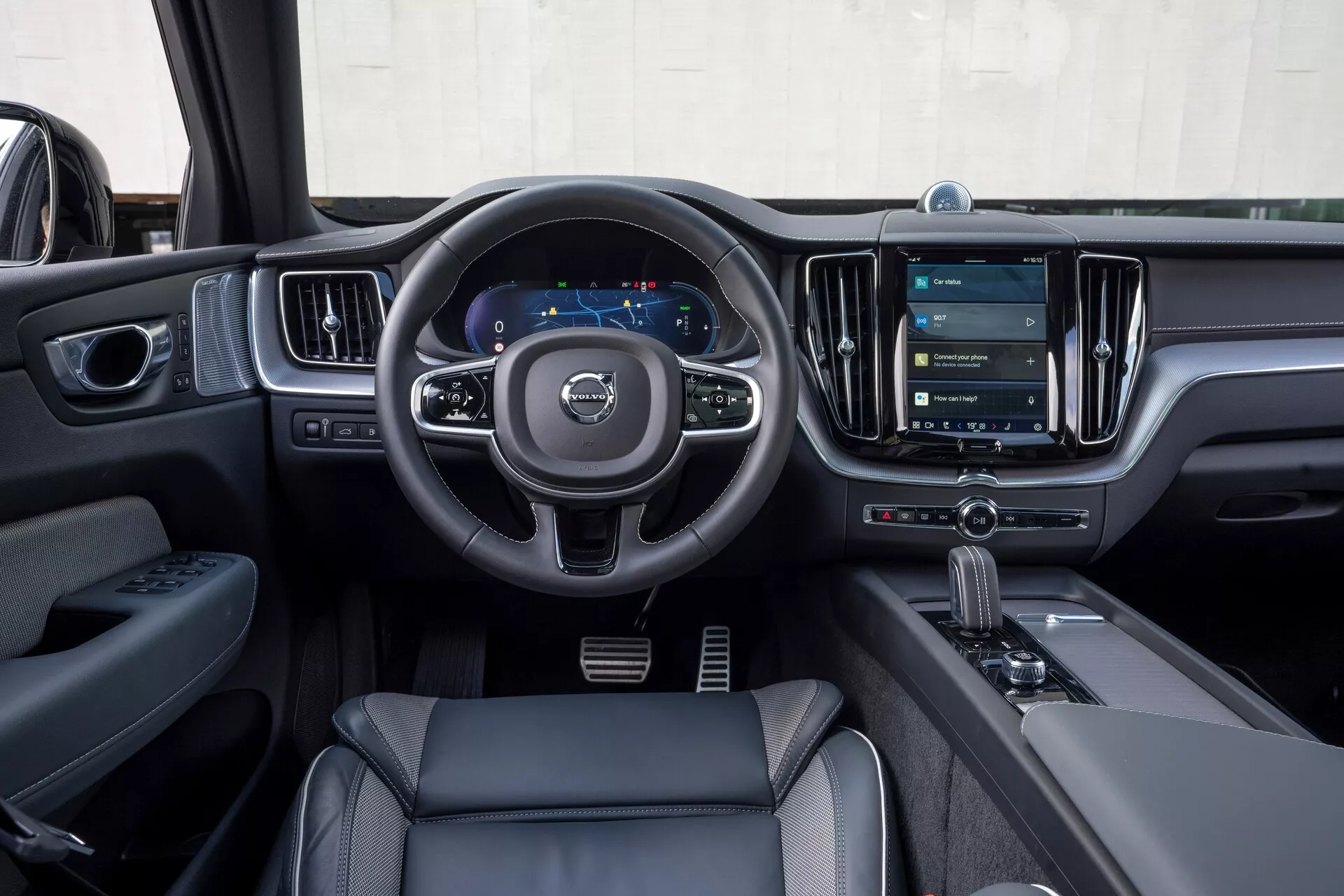 Intérieur d'un Volvo XC60 2021 (facelift de la 2e génération) depuis la perspective du conducteur. L'image met en évidence le volant à trois branches avec des boutons de commande pour l'audio, la communication et les réglages du régulateur de vitesse, un tableau de bord numérique affichant le compteur de vitesse et la navigation, et un grand système d'infodivertissement à écran tactile vertical. Les éléments de design moderne incluent des matériaux en cuir ou similicuir, des accents chromés et un levier de vitesses automatique avec sélecteur de mode de conduite. La porte du conducteur montre des commandes de fenêtres et de rétroviseurs, mettant en avant les caractéristiques technologiques et de luxe.